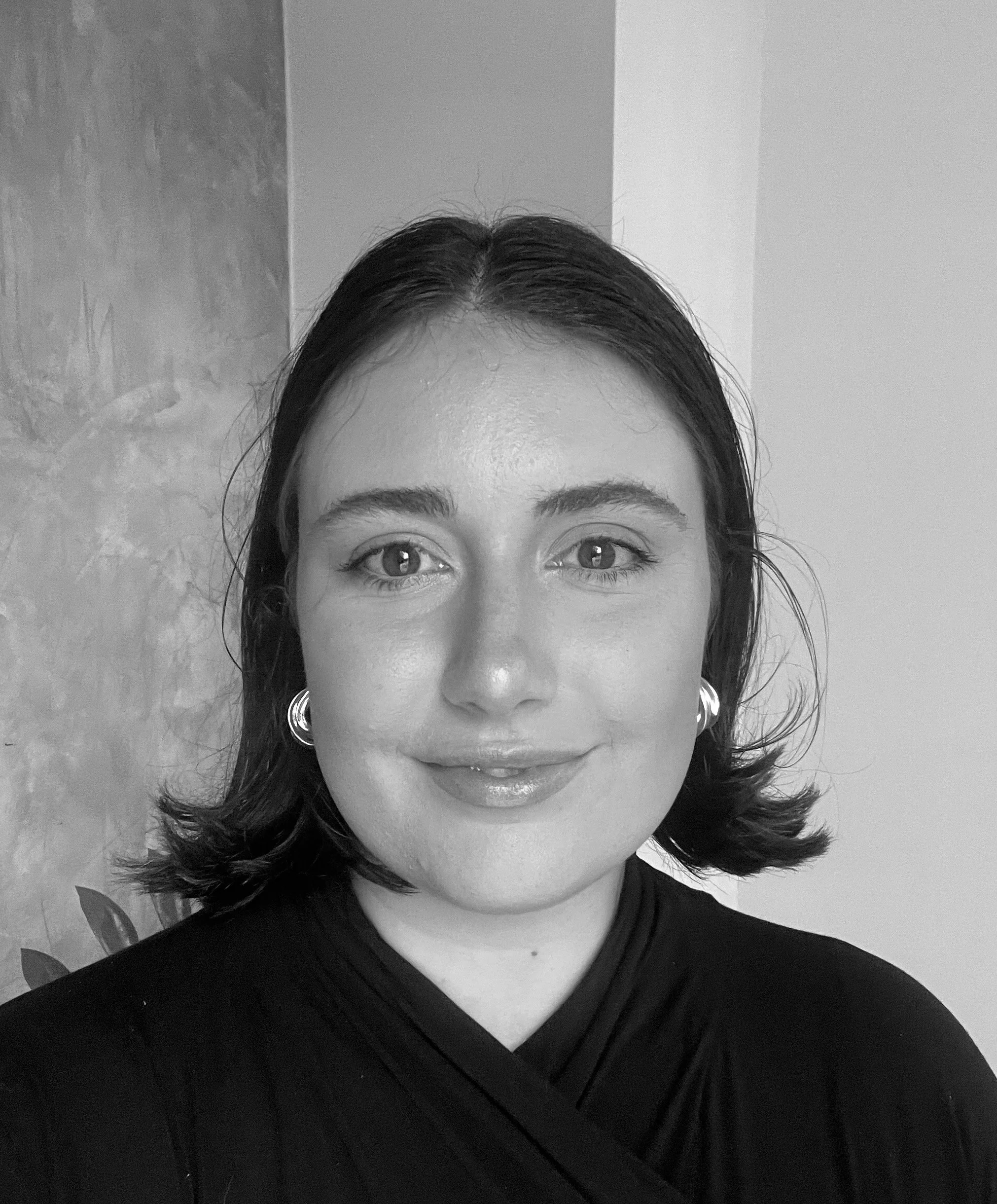 A woman with shoulder-length hair, wearing hoop earrings and a black top, smiling in a portrait photograph.