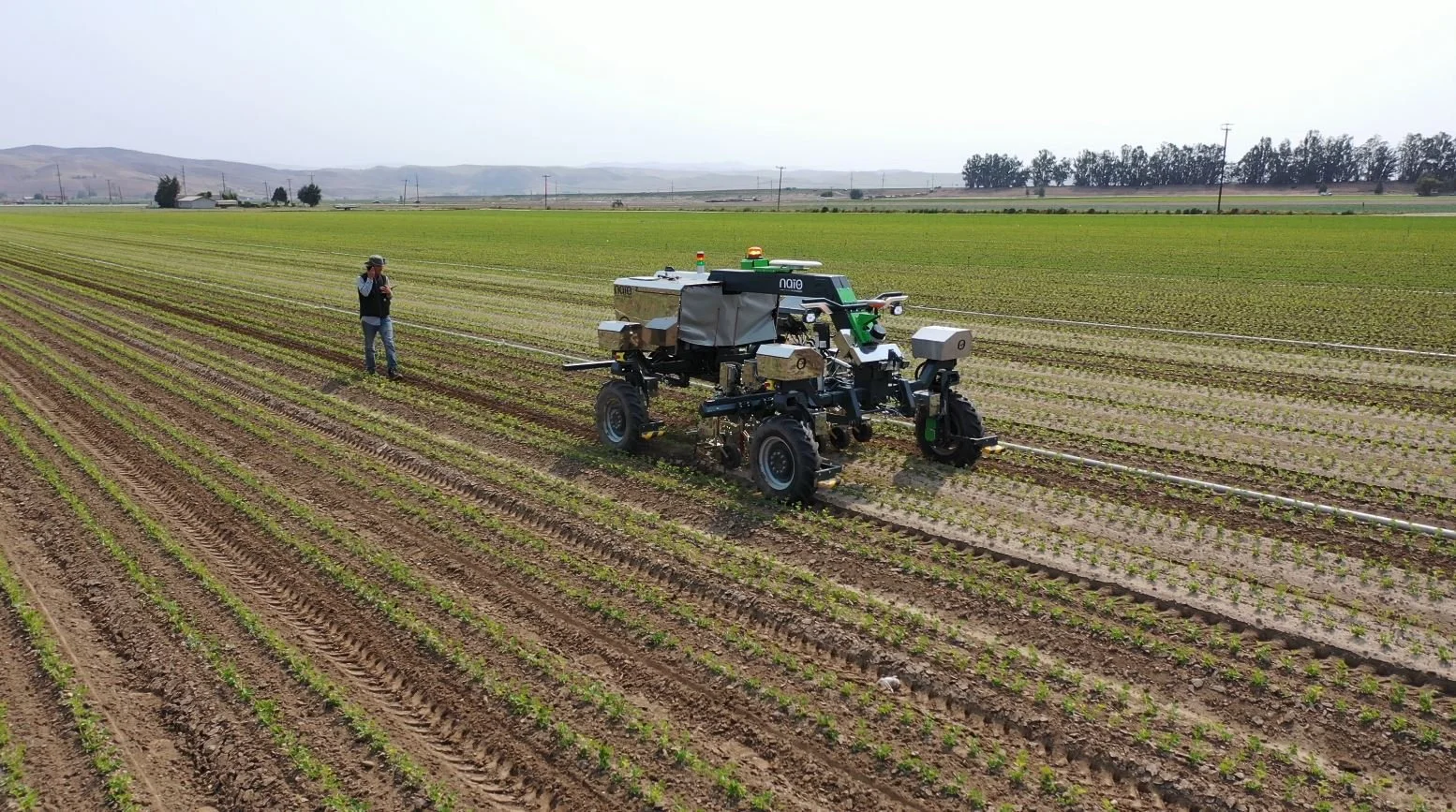Automated farming machine working in a field with a person standing nearby.