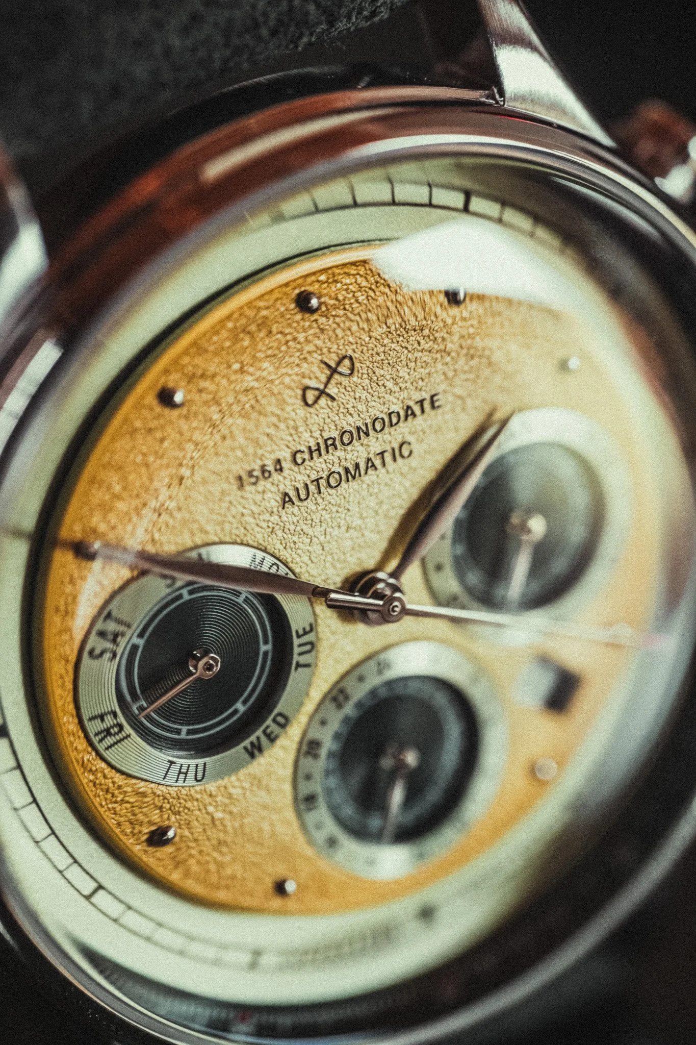 Close-up of a vintage gold-colored wristwatch face with multiple dials and black markers.