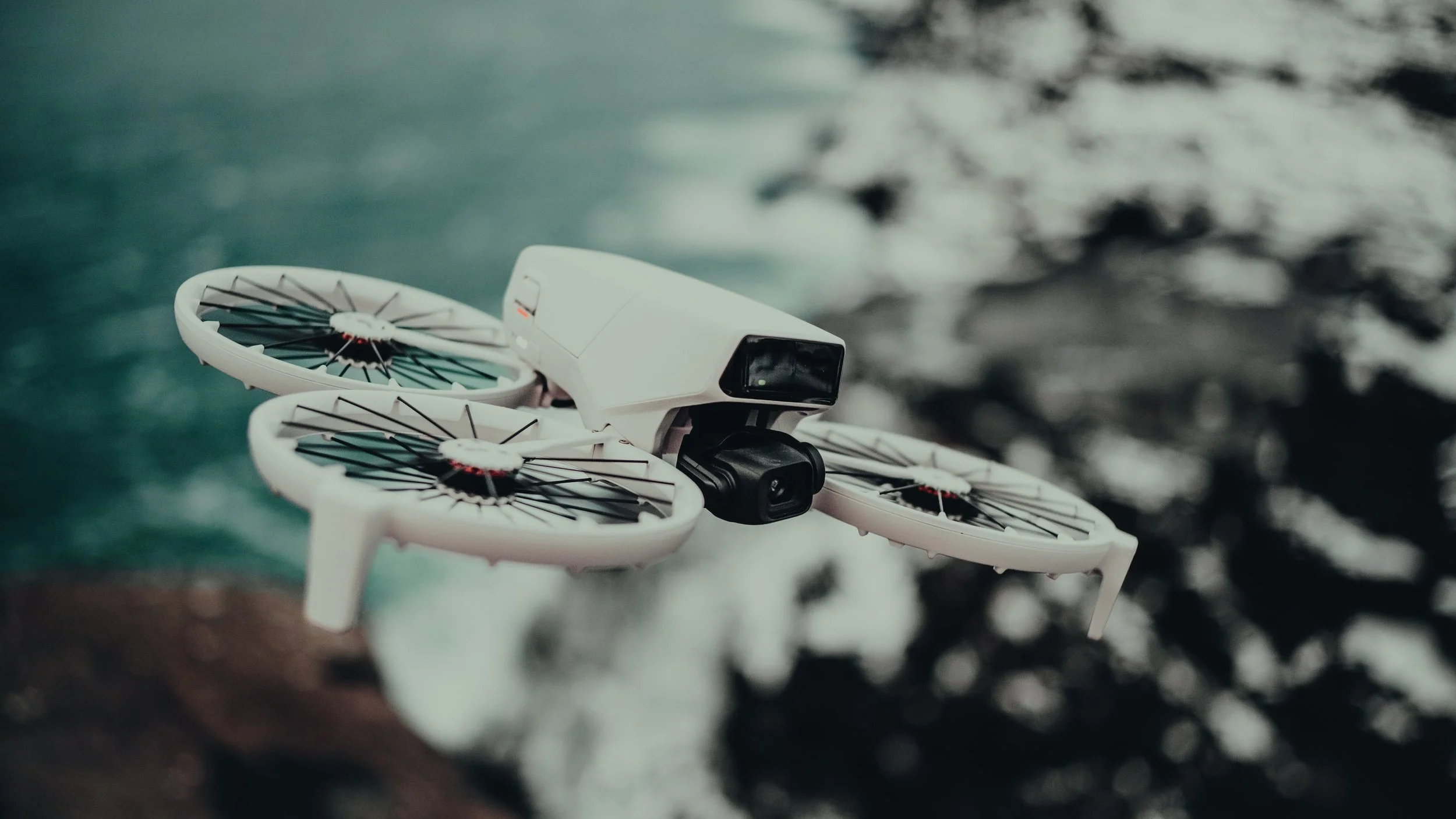A white drone flying over water with waves visible in the background.