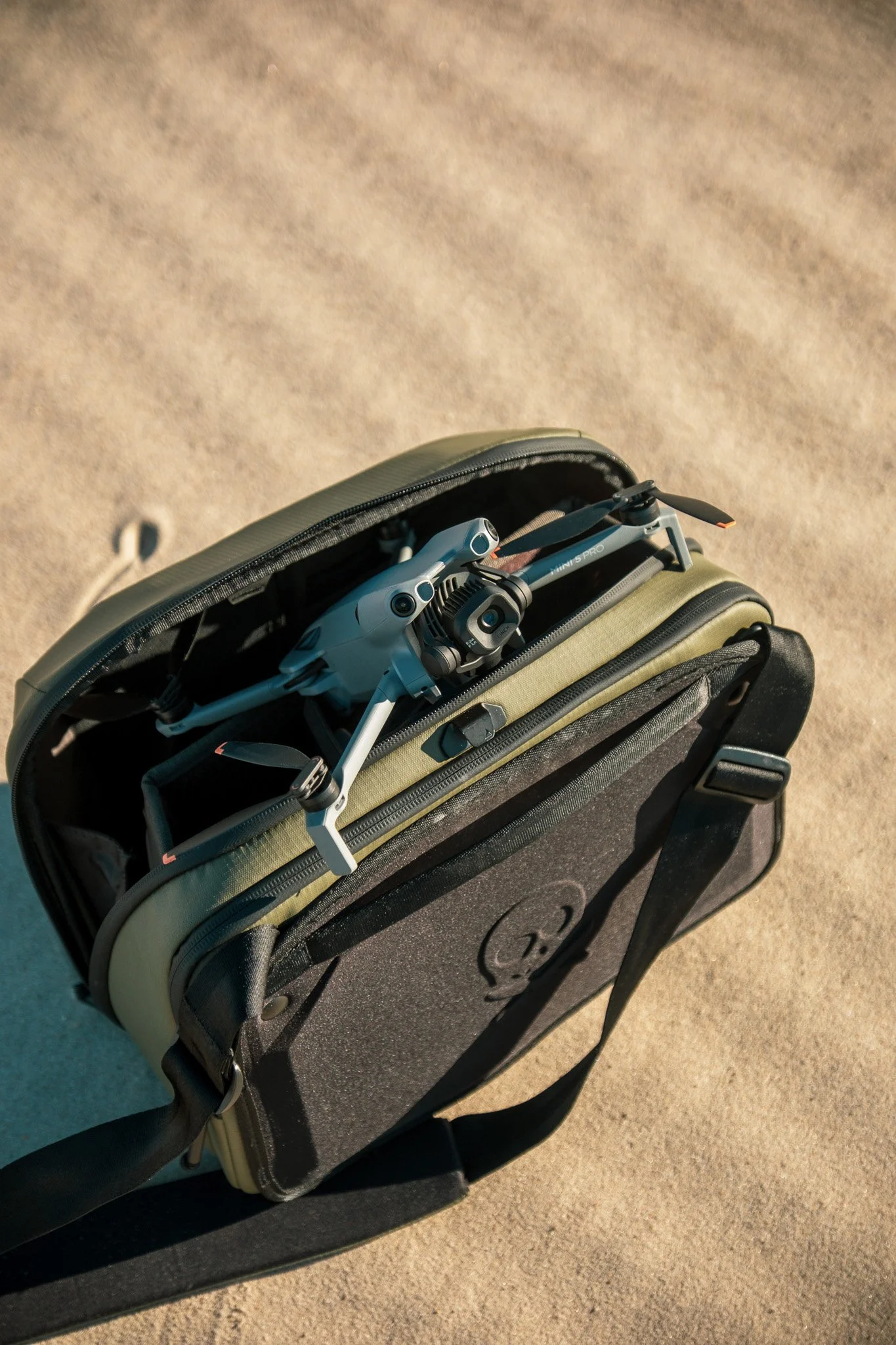 A backpack on sandy ground with a drone inside, partially visible through an open compartment.