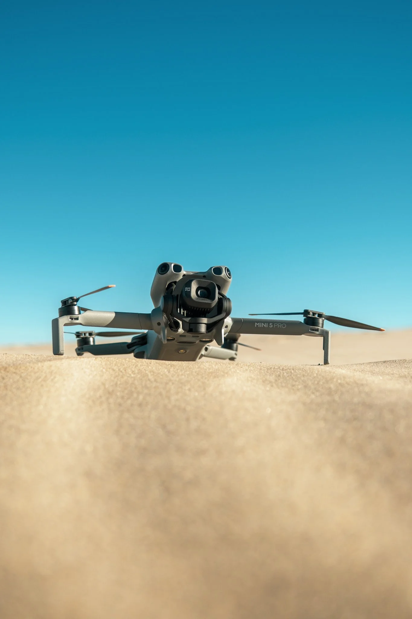 A drone on sandy desert ground under a clear blue sky.