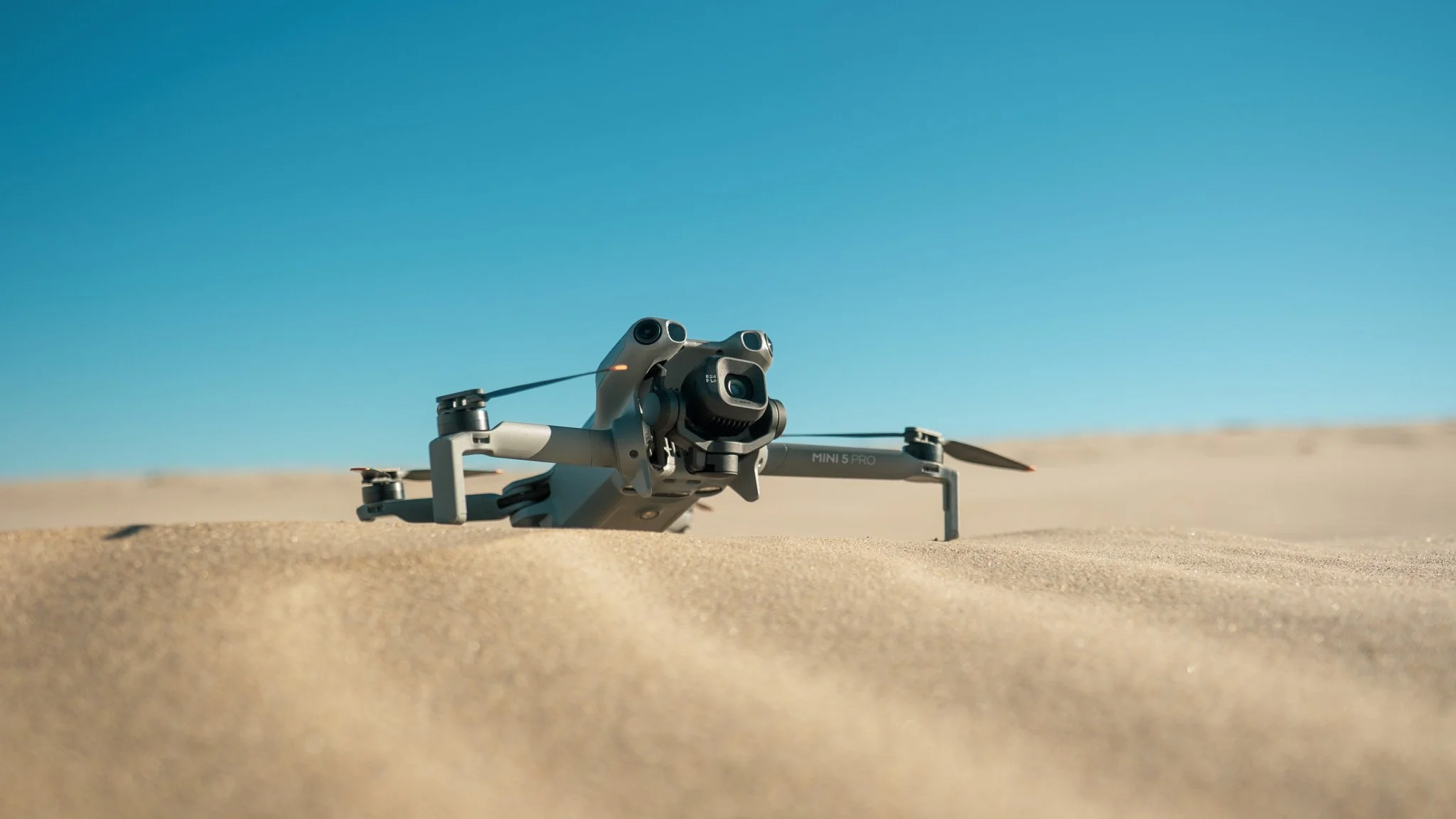 A drone resting on sand with a clear blue sky in the background.