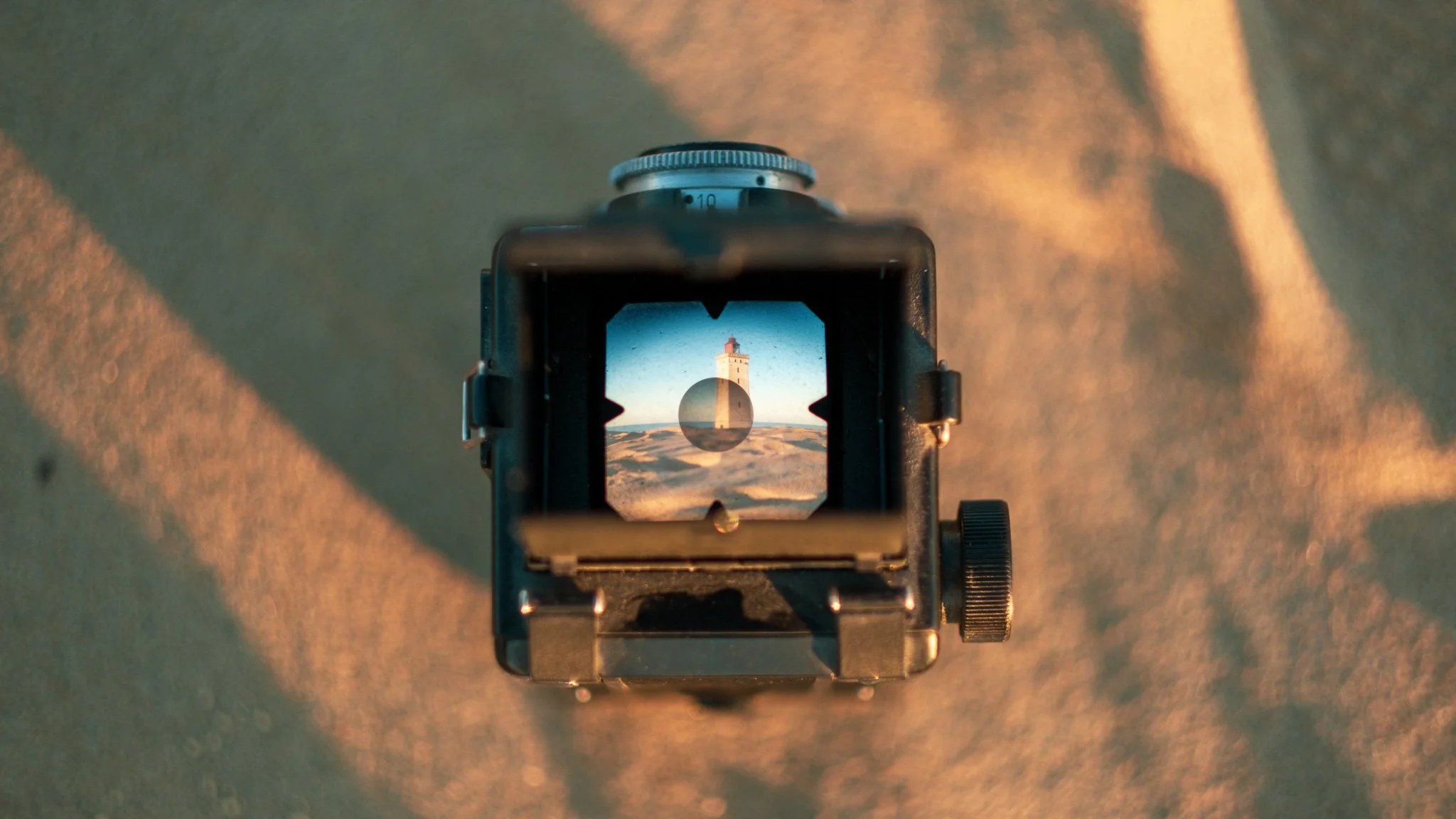 A camera viewfinder showing a lighthouse on a rocky landscape during sunset.