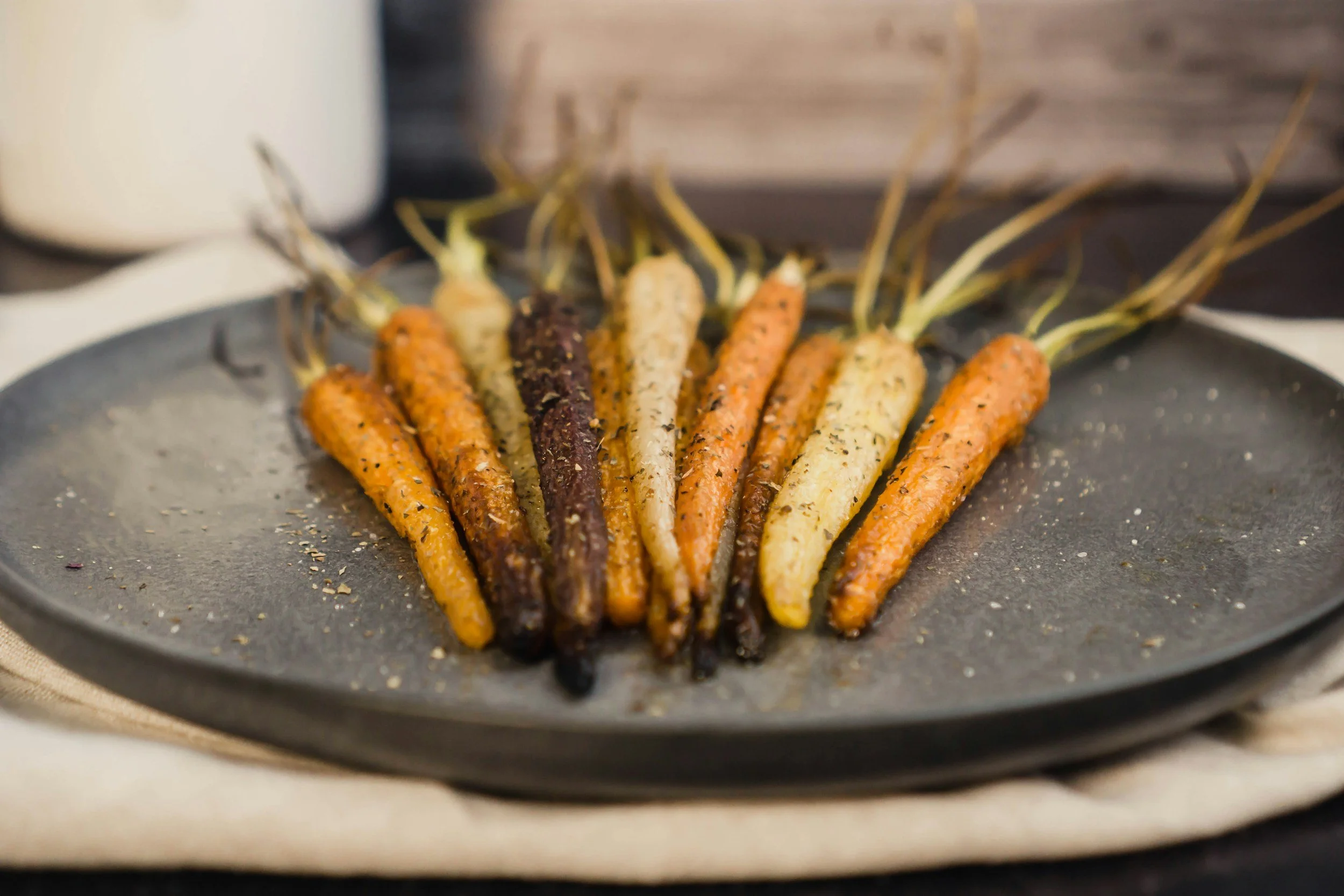 Colorful roasted carrots with varying shades of orange, yellow, purple, and white arranged on a black plate.