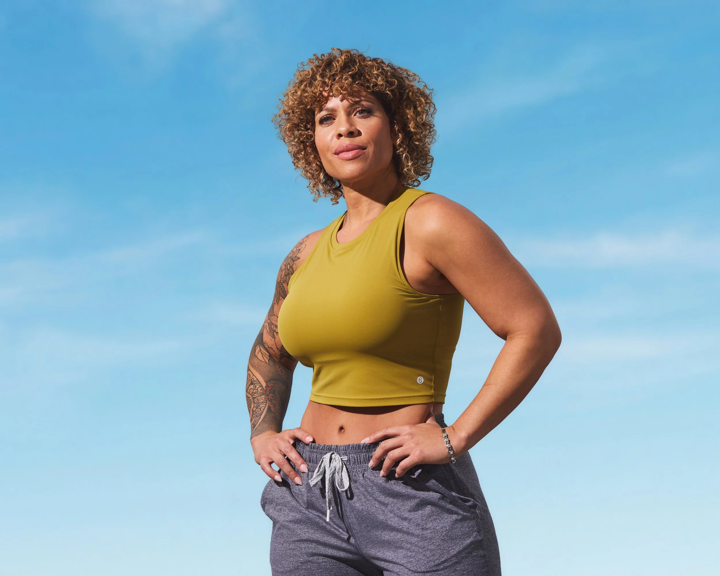 Woman in athletic wear posing under a blue sky