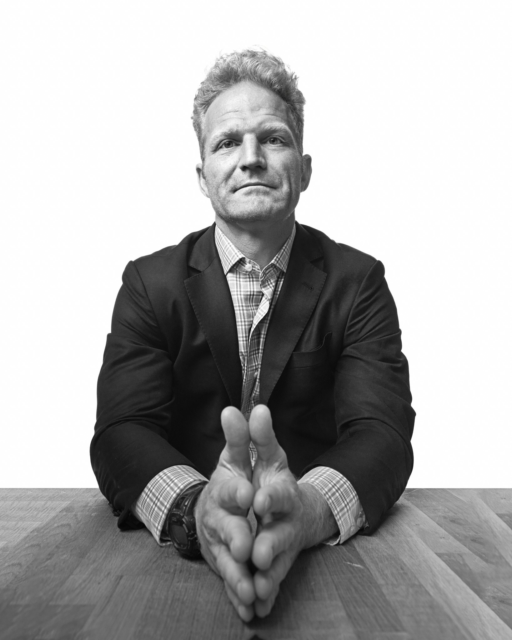 Black and white portrait of a man in a suit with hands clasped on a table.