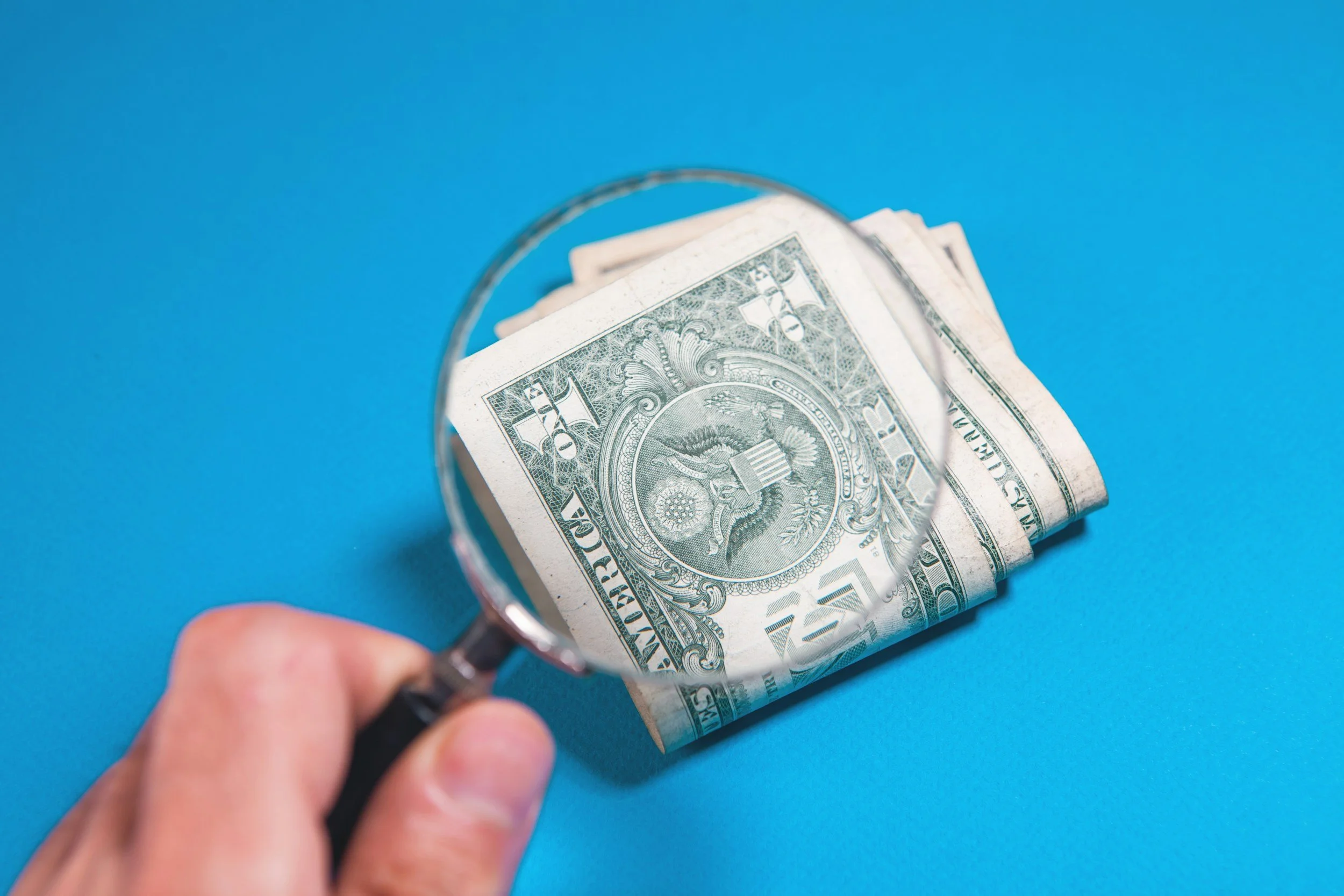 hand holding a magnifying glass over dollar bills