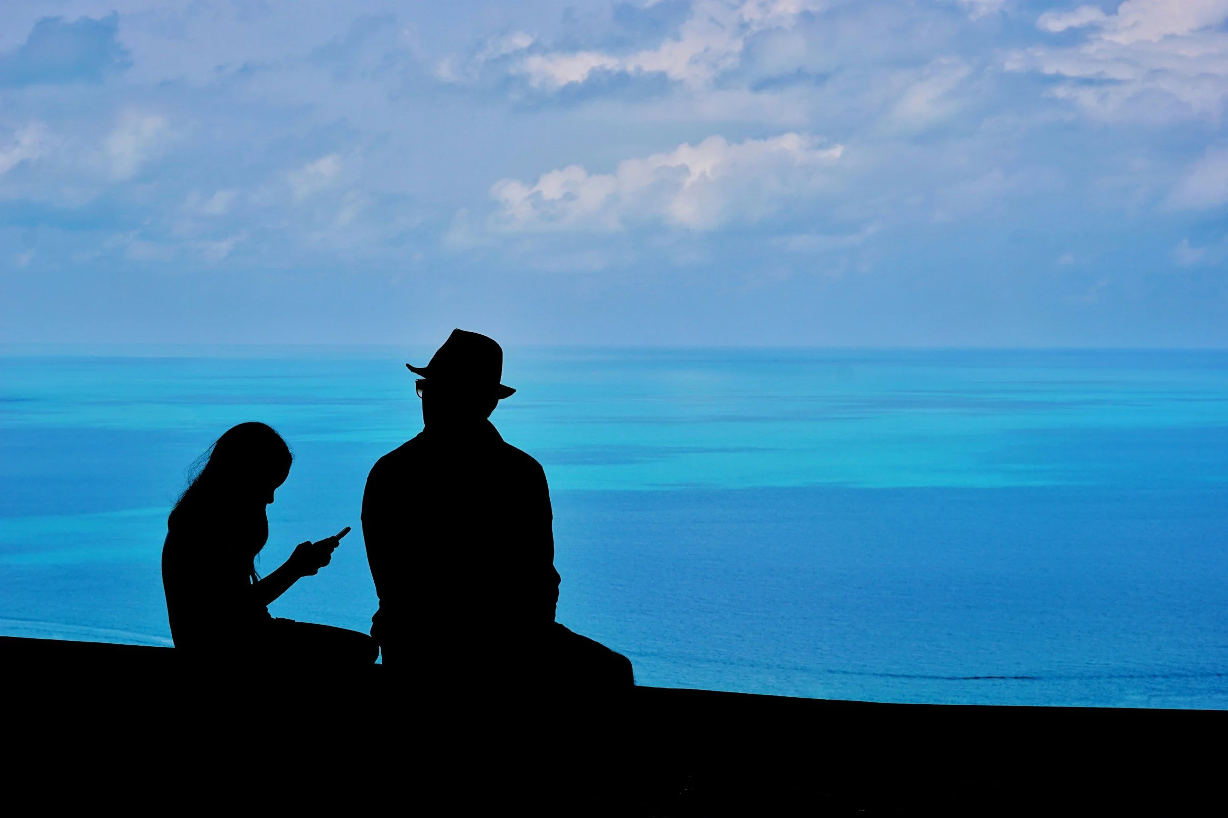 daughter on phone, sitting with father in front of ocean