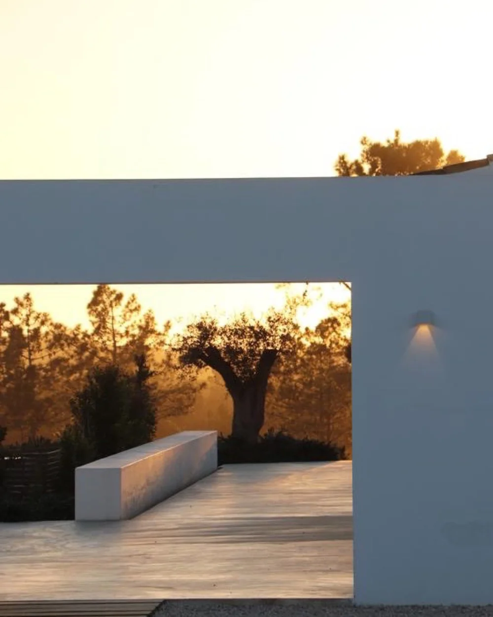 White bench and olive tree framed by Amaria’s terrace architecture in golden sunset light