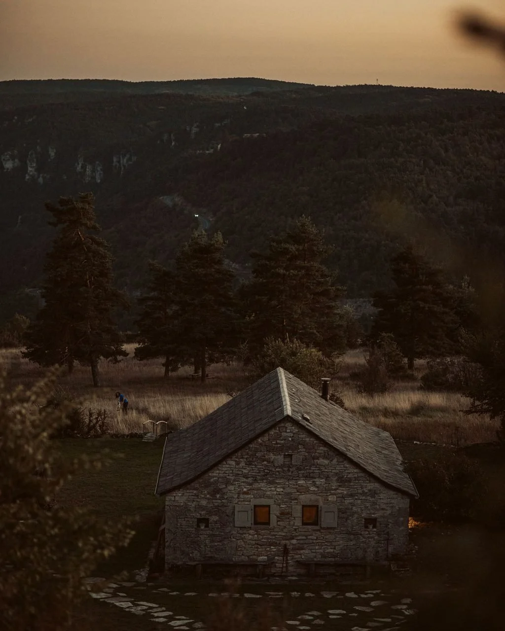Stone farmhouse at dusk with warm lit windows at L'Esprit d'Almières in the Aveyron, evening at Casa Retreats' luxury yoga retreat in southern France