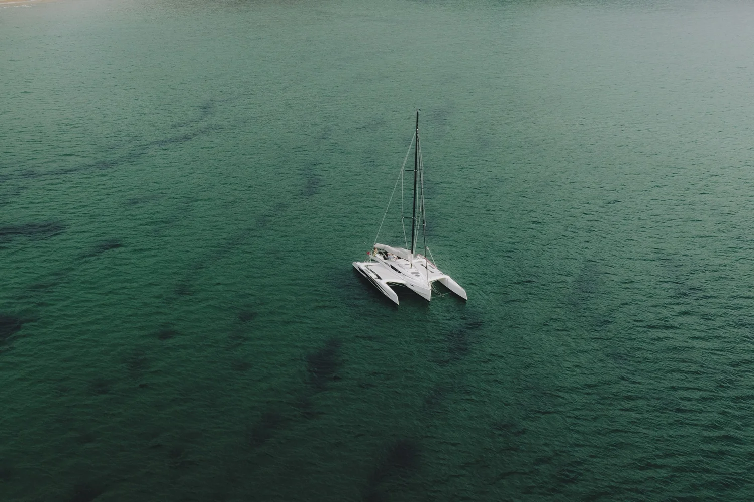Catamaran anchored in clear green water below the cliffs of Portugal&rsquo;s Costa Vicentina