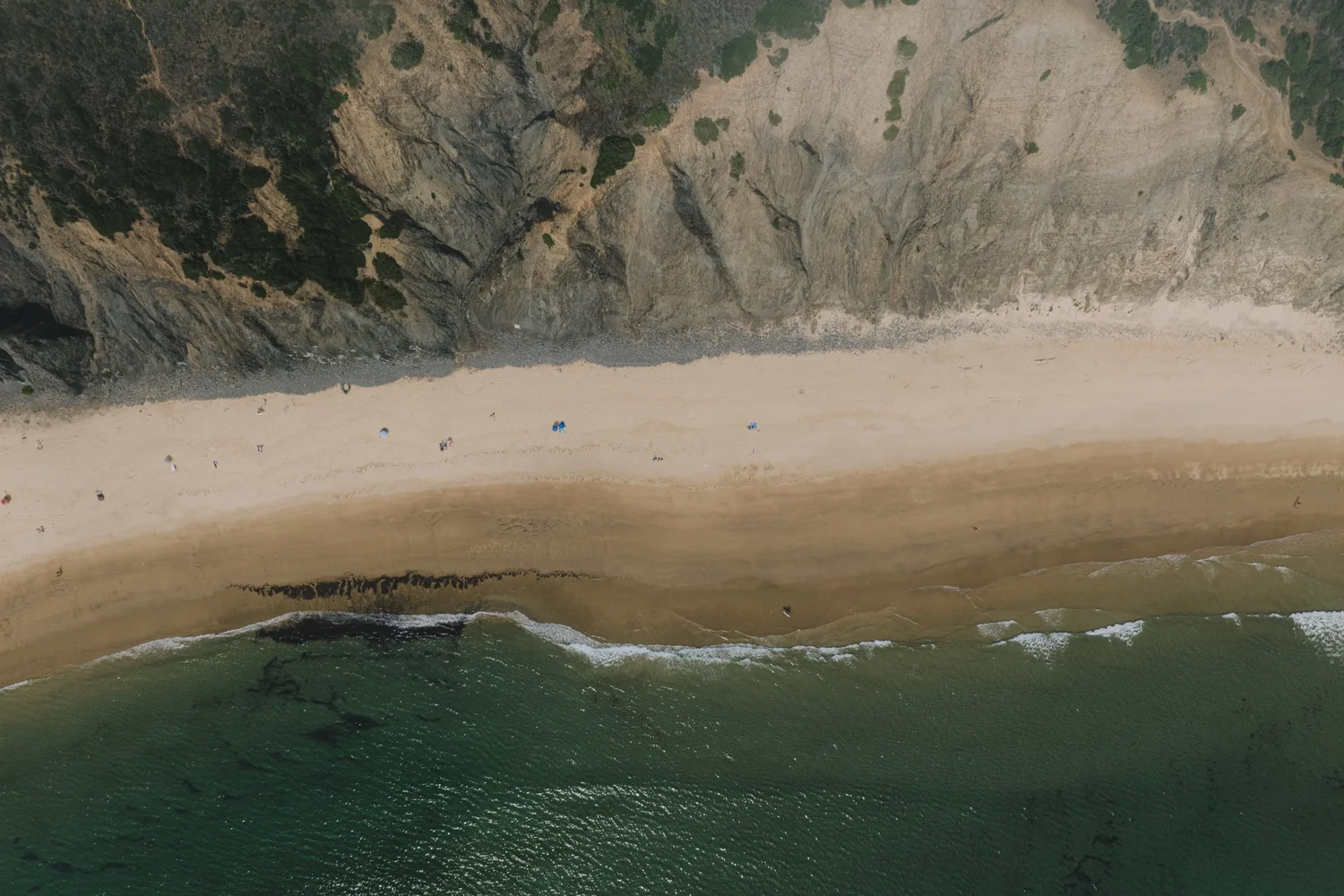 Top-down aerial view of a secluded Atlantic beach beneath high cliffs on Portugal&rsquo;s Costa Vicentina