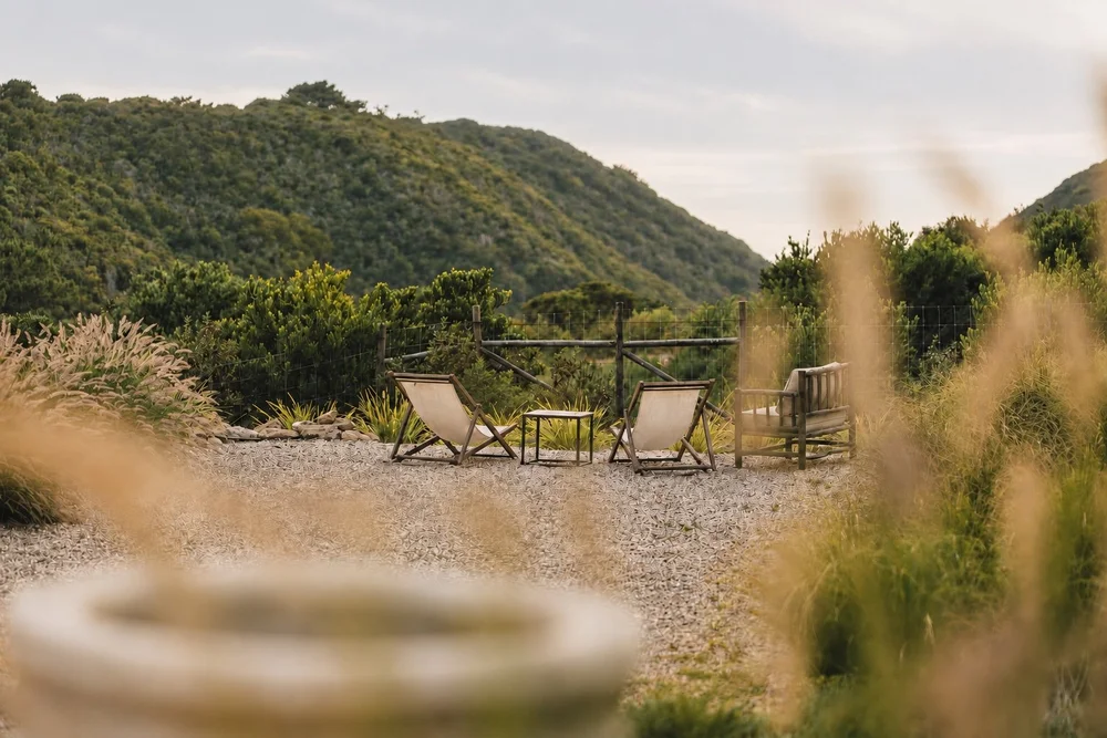 Three empty garden chairs and a small table overlooking the green valley at Amaria on Portugal’s Costa Vicentina.