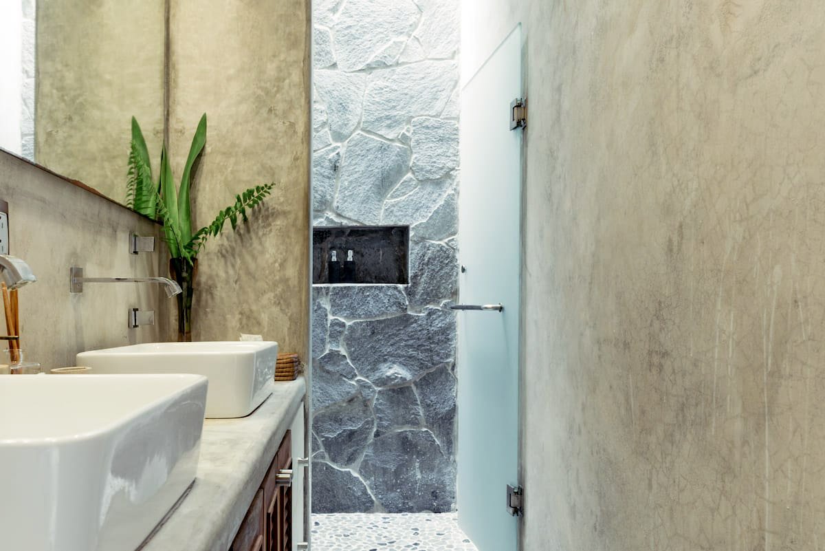 Bathroom with granite double sink, mirror, potted plant, stone wall, frosted glass door, and beige walls.