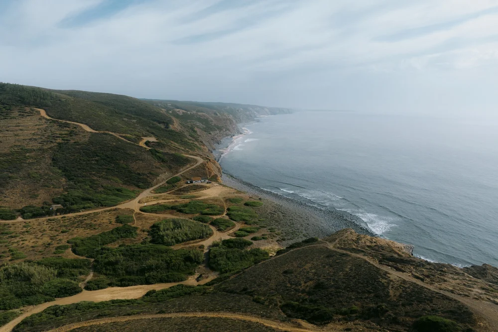 Wide aerial view of Atlantic cliffs, winding coastal tracks and shoreline along Portugal’s Costa Vicentina