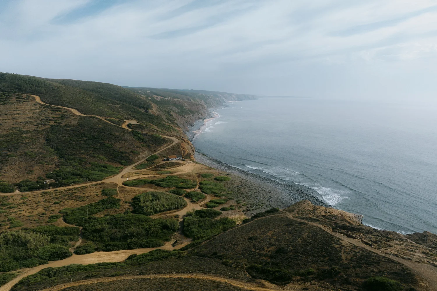 Wide aerial view of Atlantic cliffs, winding coastal tracks and shoreline along Portugal’s Costa Vicentina