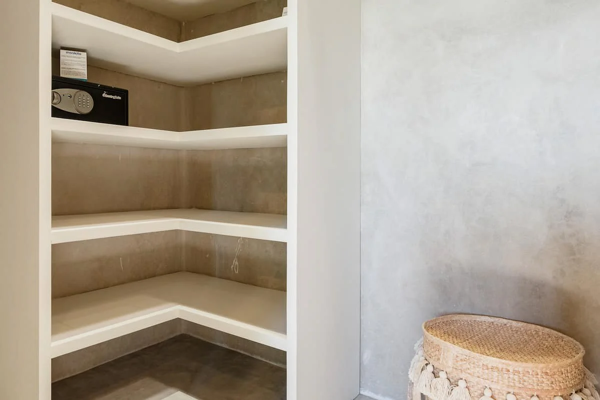 Empty built-in white shelves with a small black safe on the top shelf, next to a woven basket on the floor.