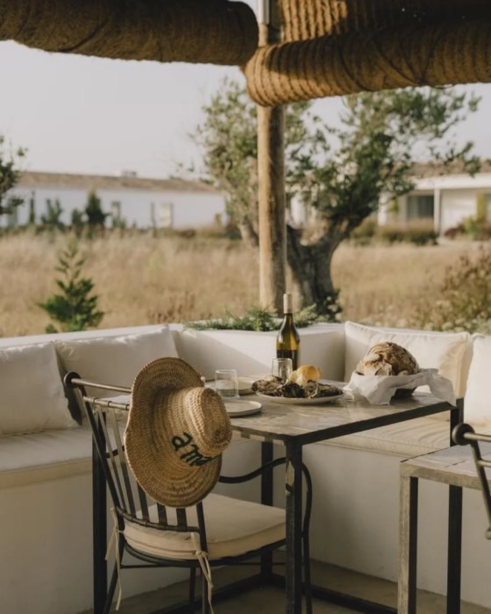 Oysters, bread and wine set on an outdoor banquette beneath a woven shade at Amaria in Portugal