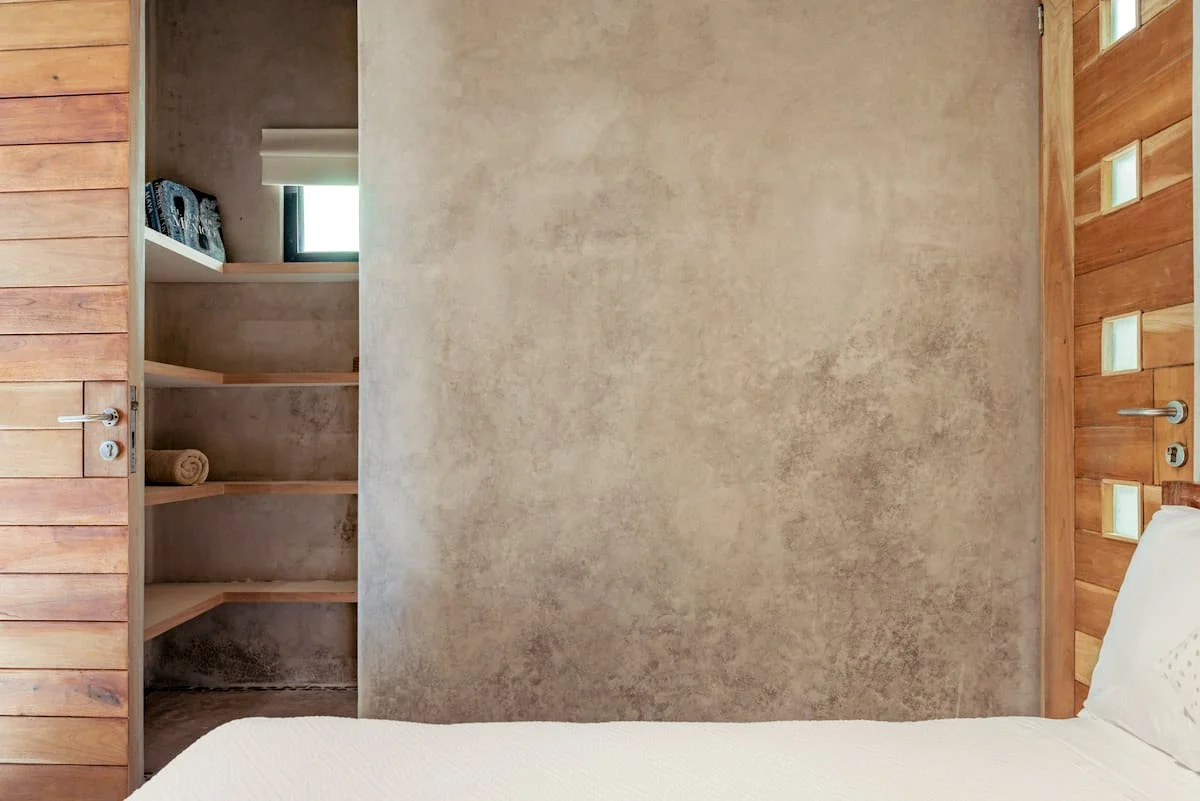 Part of a bedroom with a wooden door and built-in shelves, a small window, and a white bed with pillows.