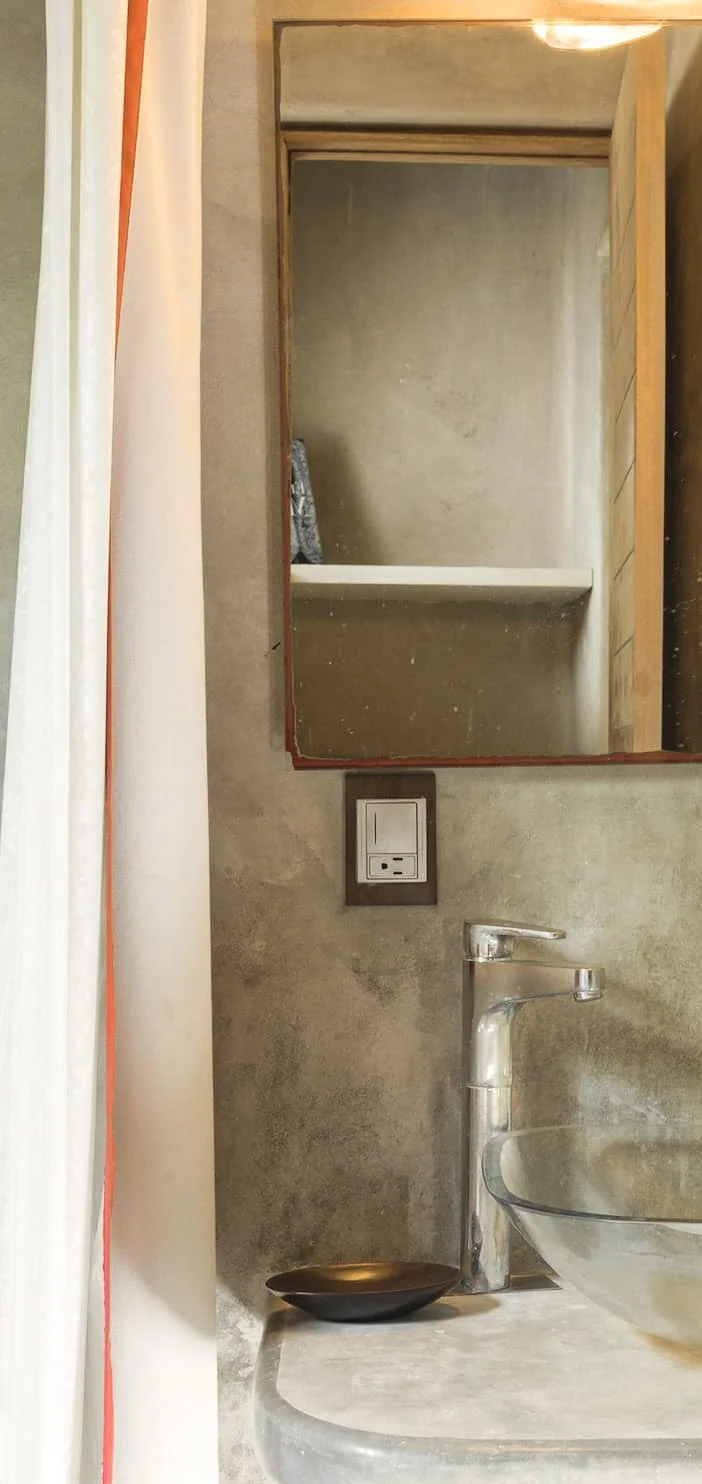 Close-up view of a bathroom vanity area with a mirror, a modern faucet, a glass bowl sink, and a light switch on a textured wall.
