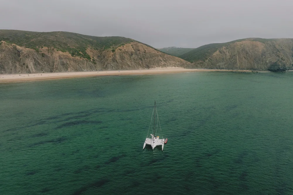 Aerial view of a white catamaran in a sheltered Atlantic bay beneath cliffs on Portugal’s southwest coast