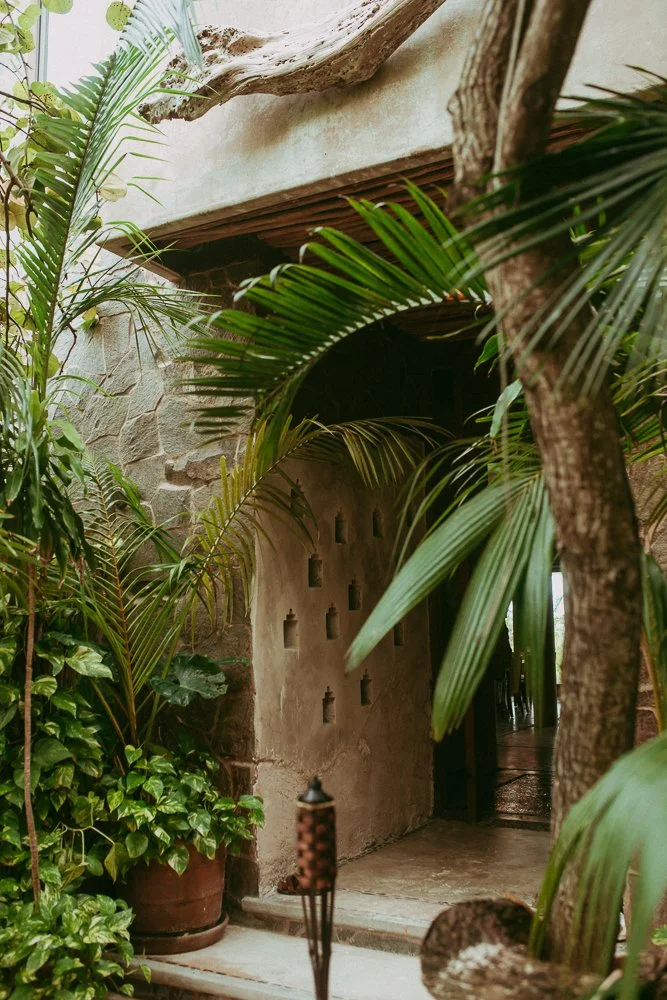 Luxury yoga and wellness retreats in Tulum, Mexico — stone entry framed by palms at Casa Maya Ka’an, welcoming path to a calm, eco-luxury setting.