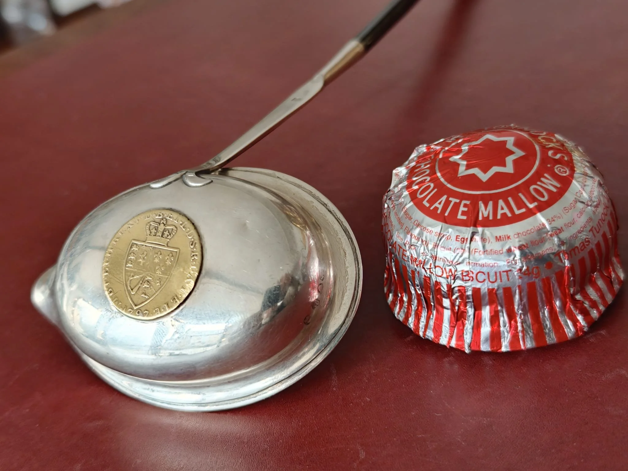 A silver coin and a wrapped chocolate candy on a red surface.