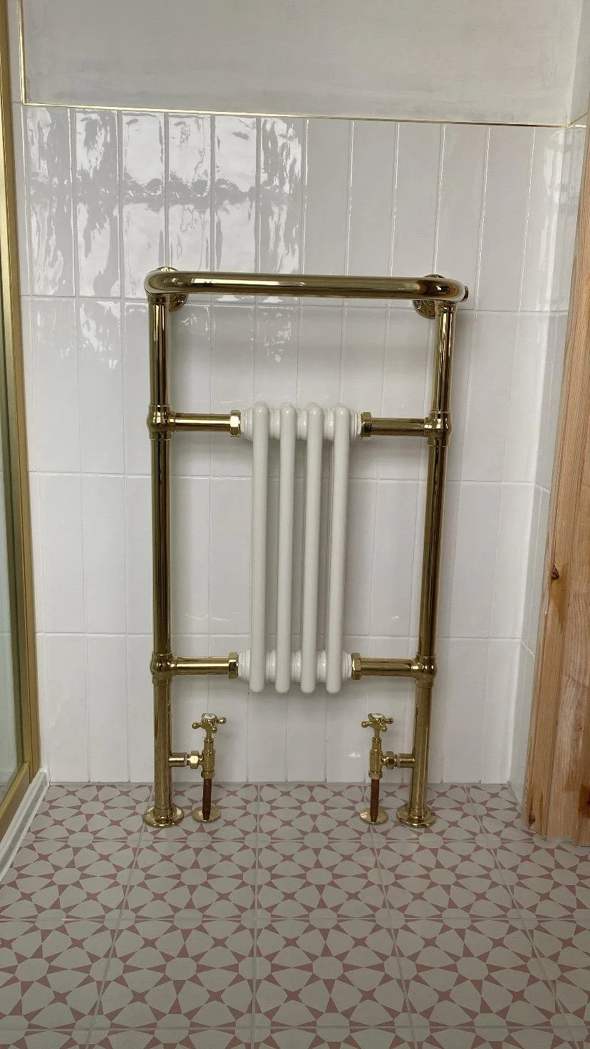 A decorative radiator with gold piping and white radiator bars is mounted on a tiled wall in a bathroom.