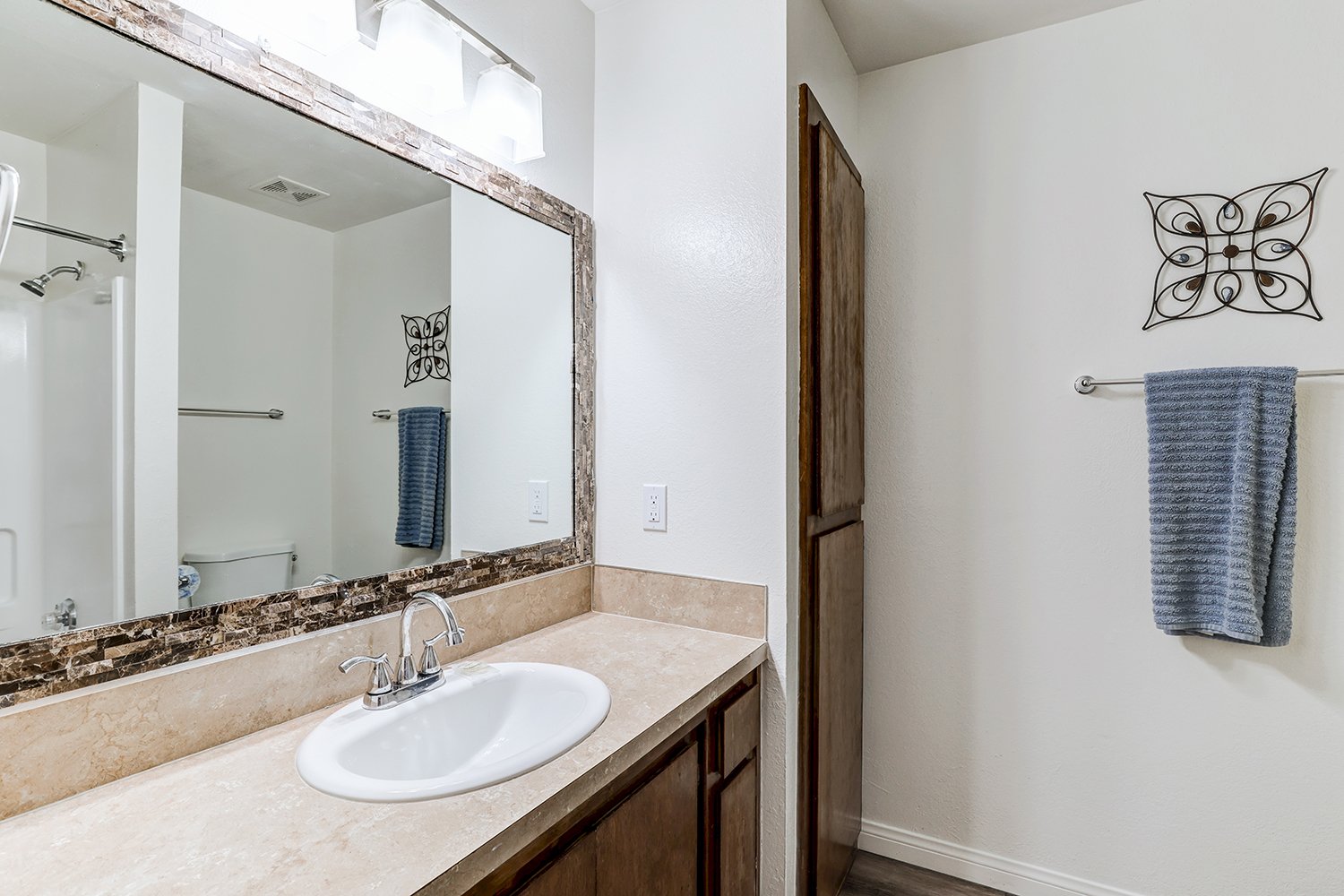 This photo includes the bright bathroom interior featuring a dark wood vanity cabinet with a beige countertop and a white sink.