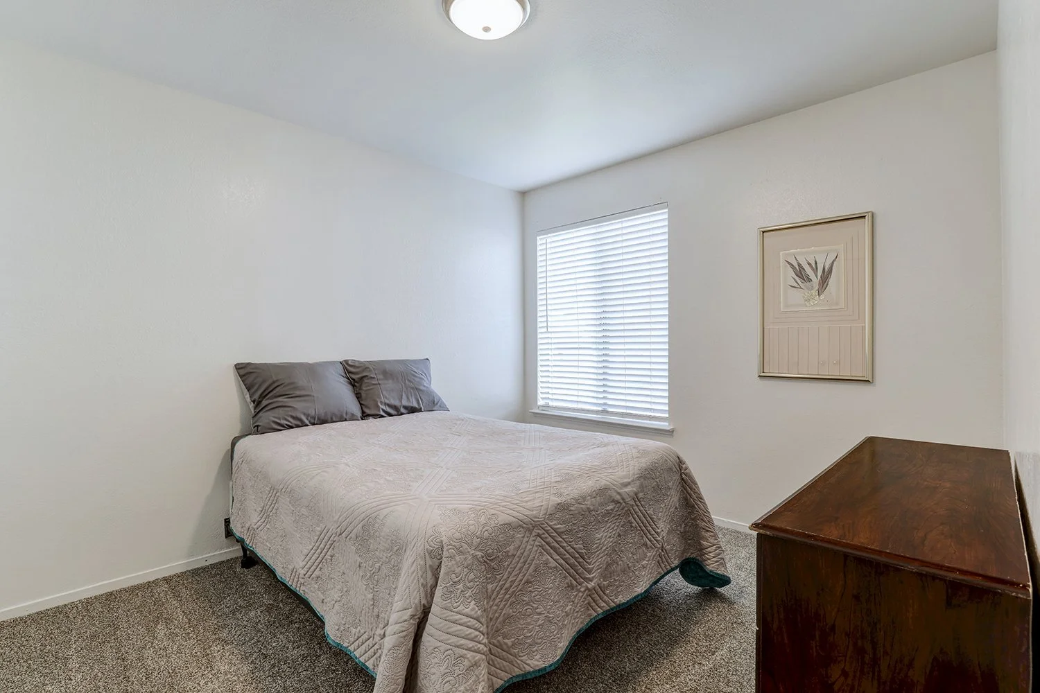 Another view of a bedroom that features a wooden dresser and artwork. 