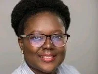 Portrait of a woman with short curly hair, wearing glasses and earrings, smiling at the camera.