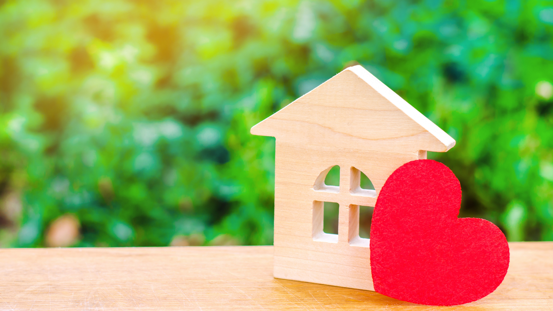 wooden cutout of a home with a red heart, against a green background