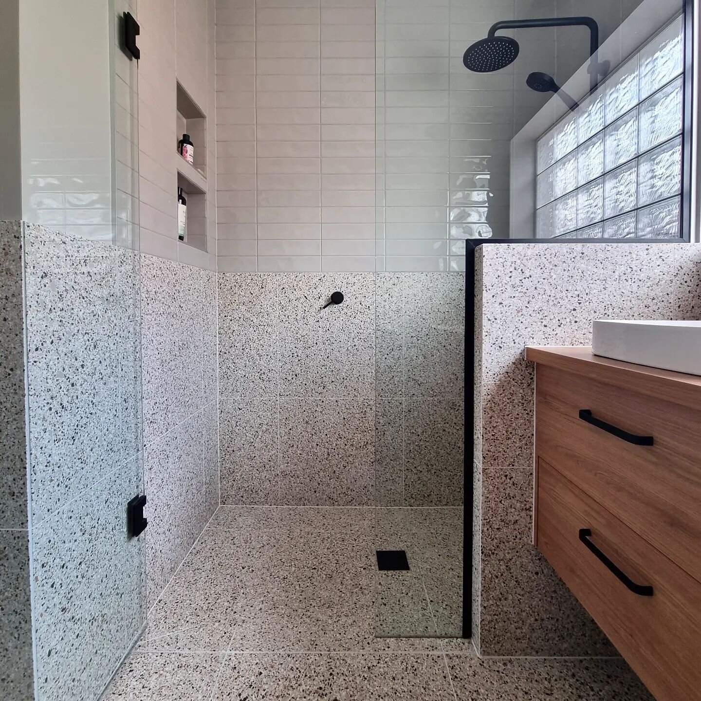 Terrazzo continues! There are so many elements to this bathroom that we love - the original glass brick window, continuing the terrazzo tile from the floor to the walls around the entire room, the beige subways &amp; walls to the black fittings. Oooo