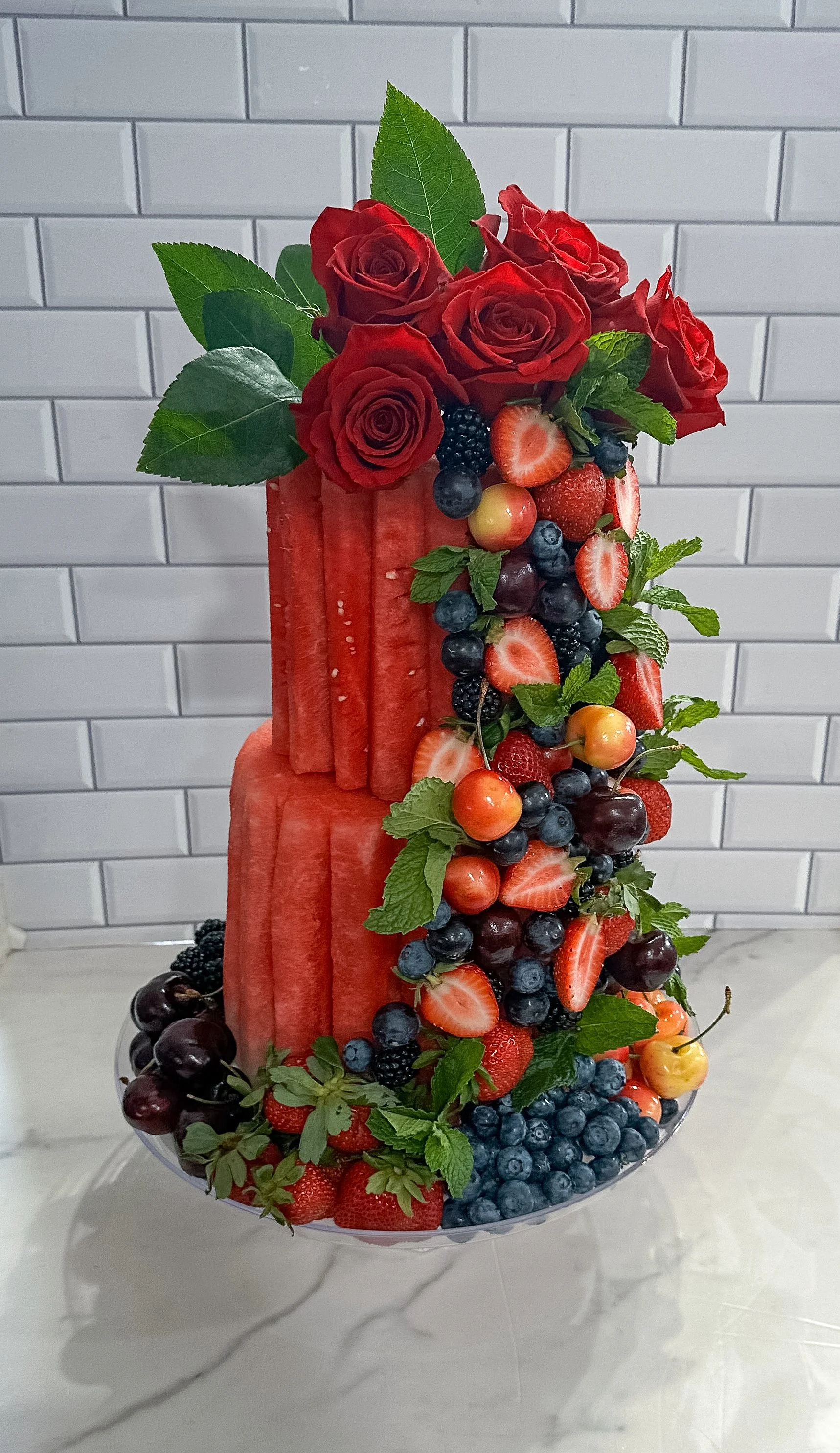 Fresh two-tier watermelon fruit cake display with berries, edible flowers and topped with fresh roses