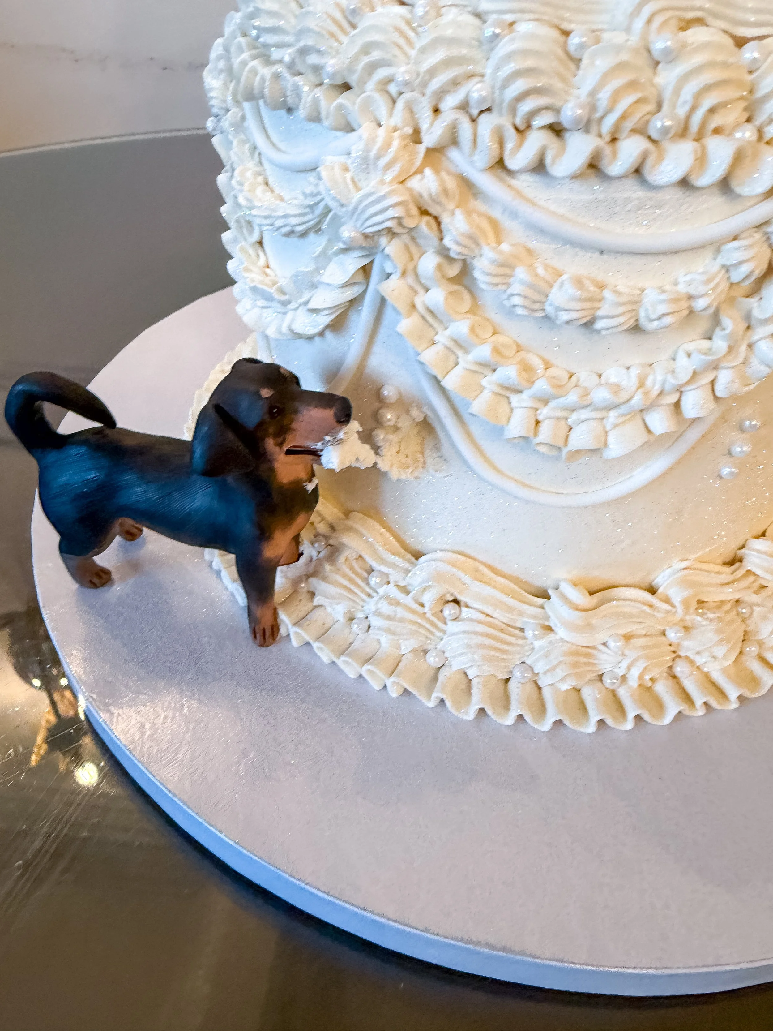 Vegan three-tier mini wedding cake with a dog topper. The dog is eating a piece of the cake 