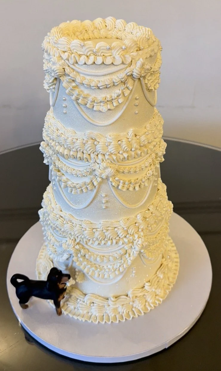 Three-tier vegan mini wedding cake with a dog statue. The dog statue is taking a bite off the side of the wedding cake