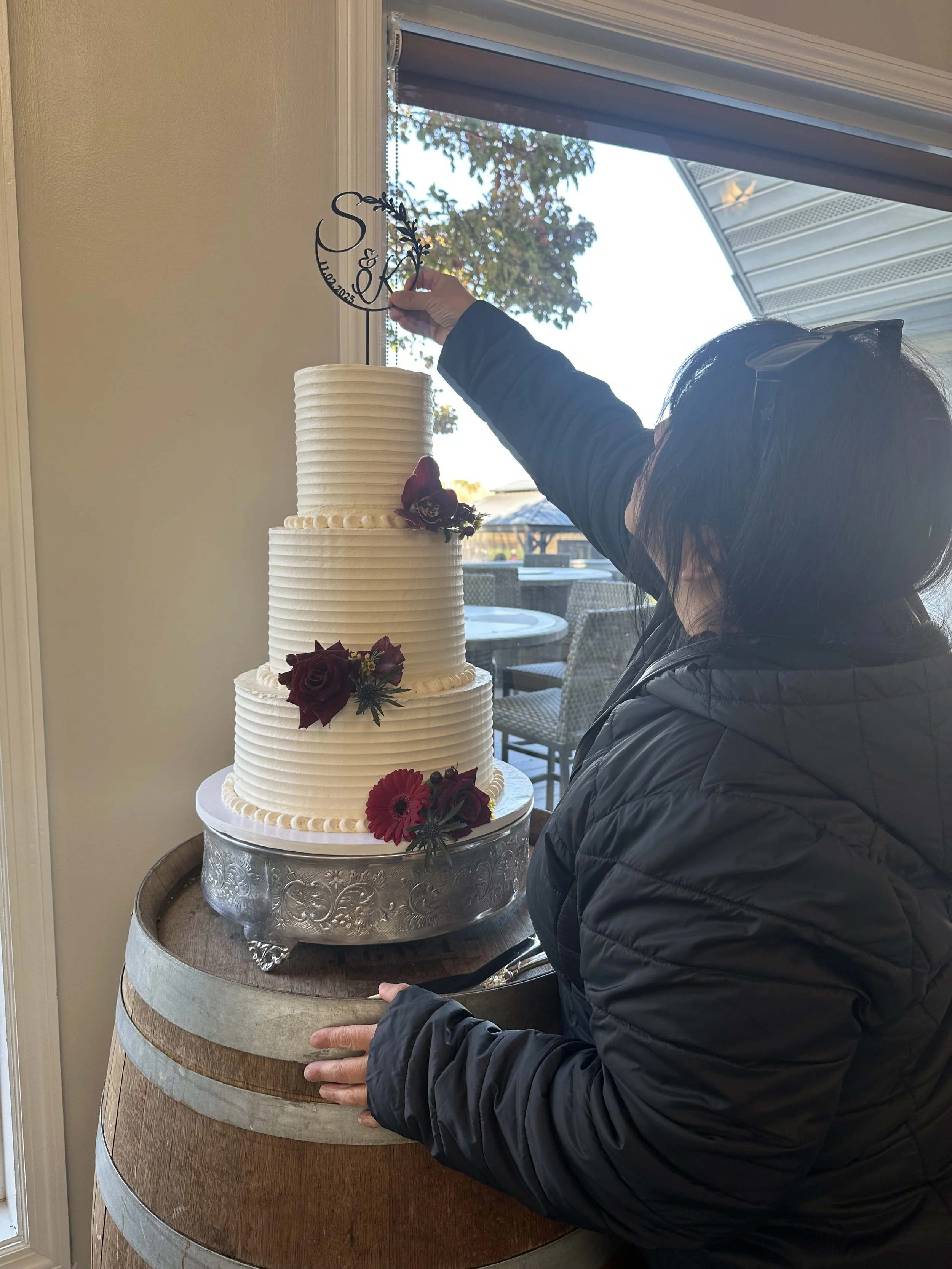 Behind the scenes of a vegan wedding cake setup at Swan Lake Caterers in Manorville, NY placing the cake topper on a custom three-tier wedding cake