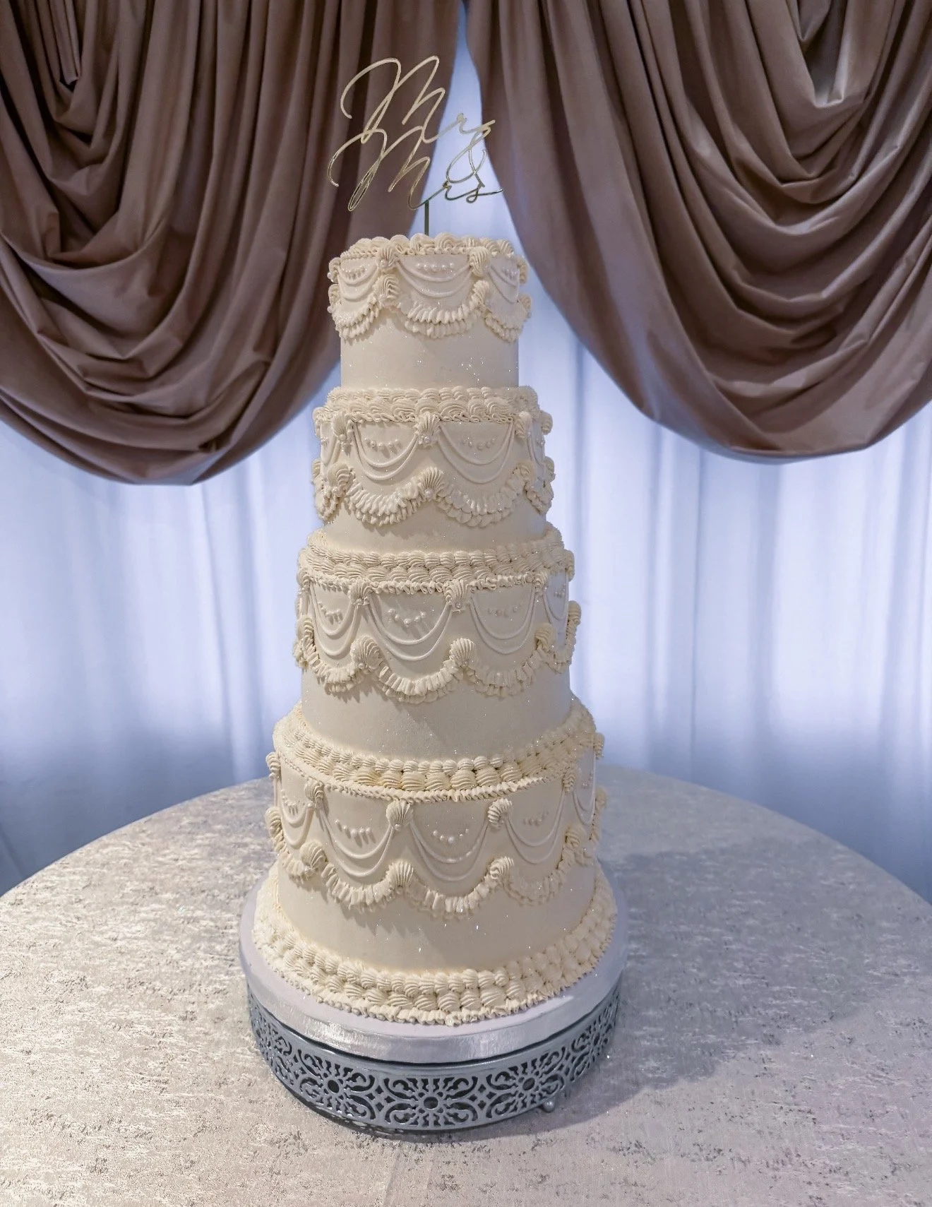 Four-tier vegan vintage wedding cake featuring intricate Lambeth piping, elegant draped buttercream swags, edible pearls, and romantic detailing, created by Veg on Board for a wedding at Mill River Club in Oyster Bay, Long Island NY