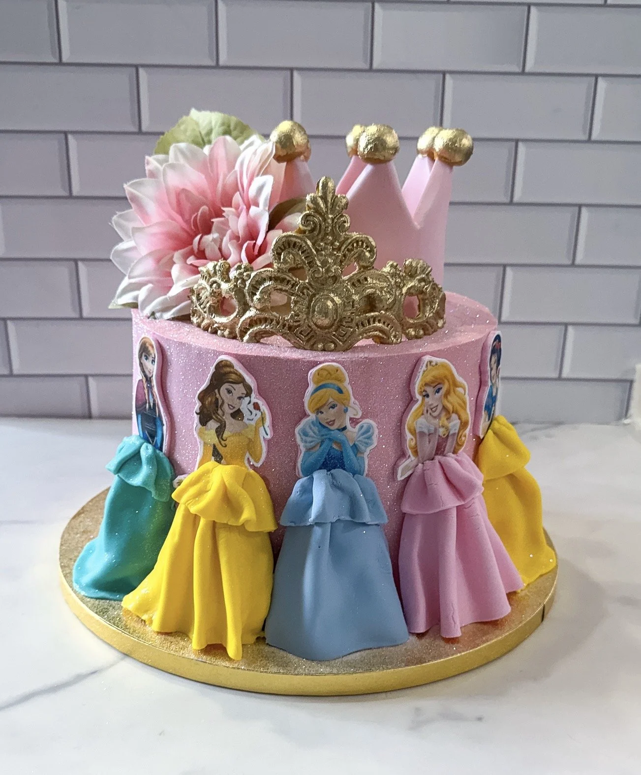 Vegan princess themed birthday cake with fondant crowns and princess skirts topped with pink flowers