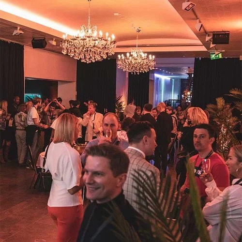 Mennesker samlet på et sosialt arrangement i et rom med lysekroner og mørke gardiner hos Oslo Event Hub.