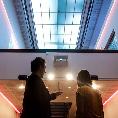 To personer står i en moderne bygning med glasskuppel i taket, med lysende kanter langs taket og taket av bygningen.