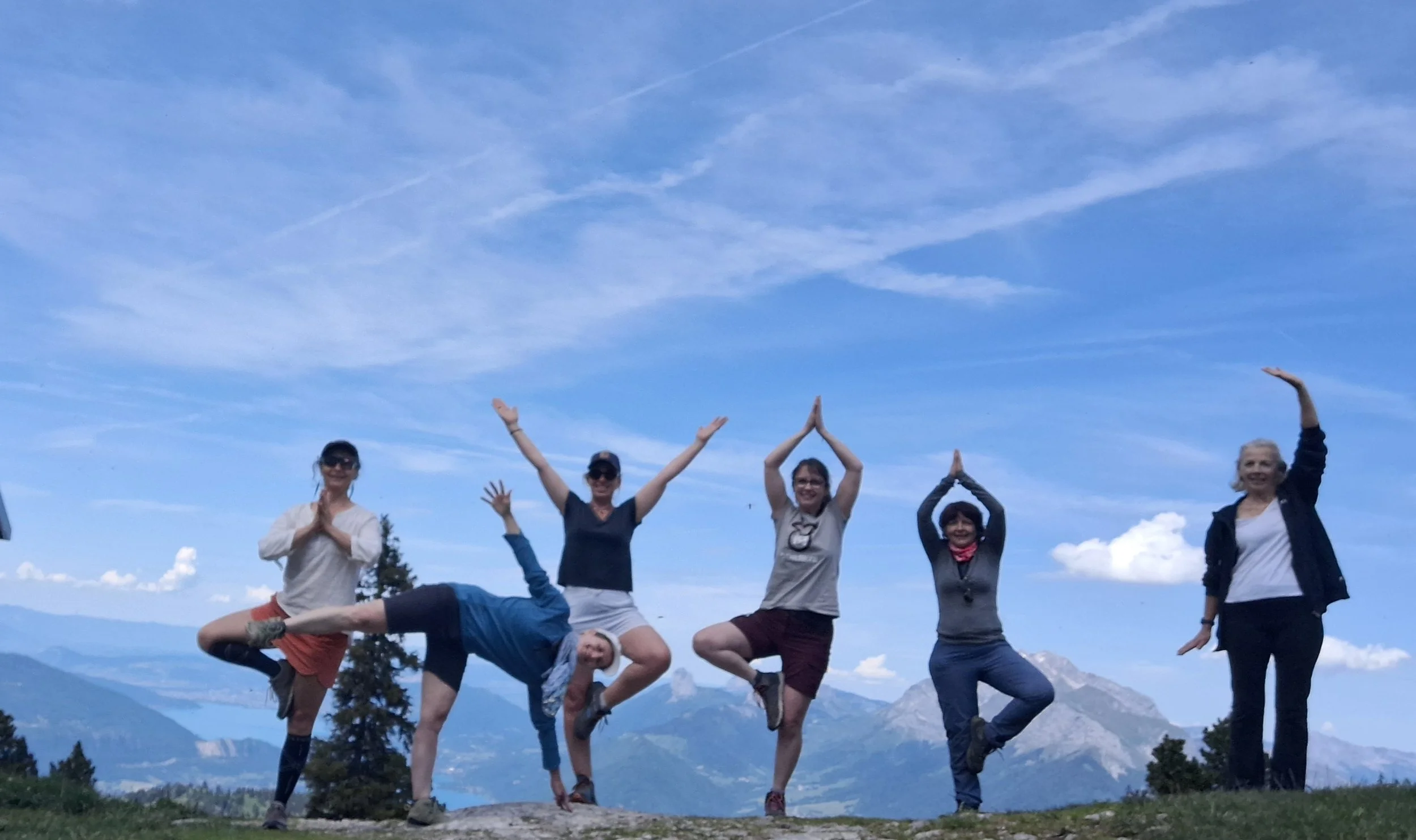 Un groupe de personnes pratiquant le yoga en plein air dans une clairière entourée d'arbres, sous un ciel ensoleillé.