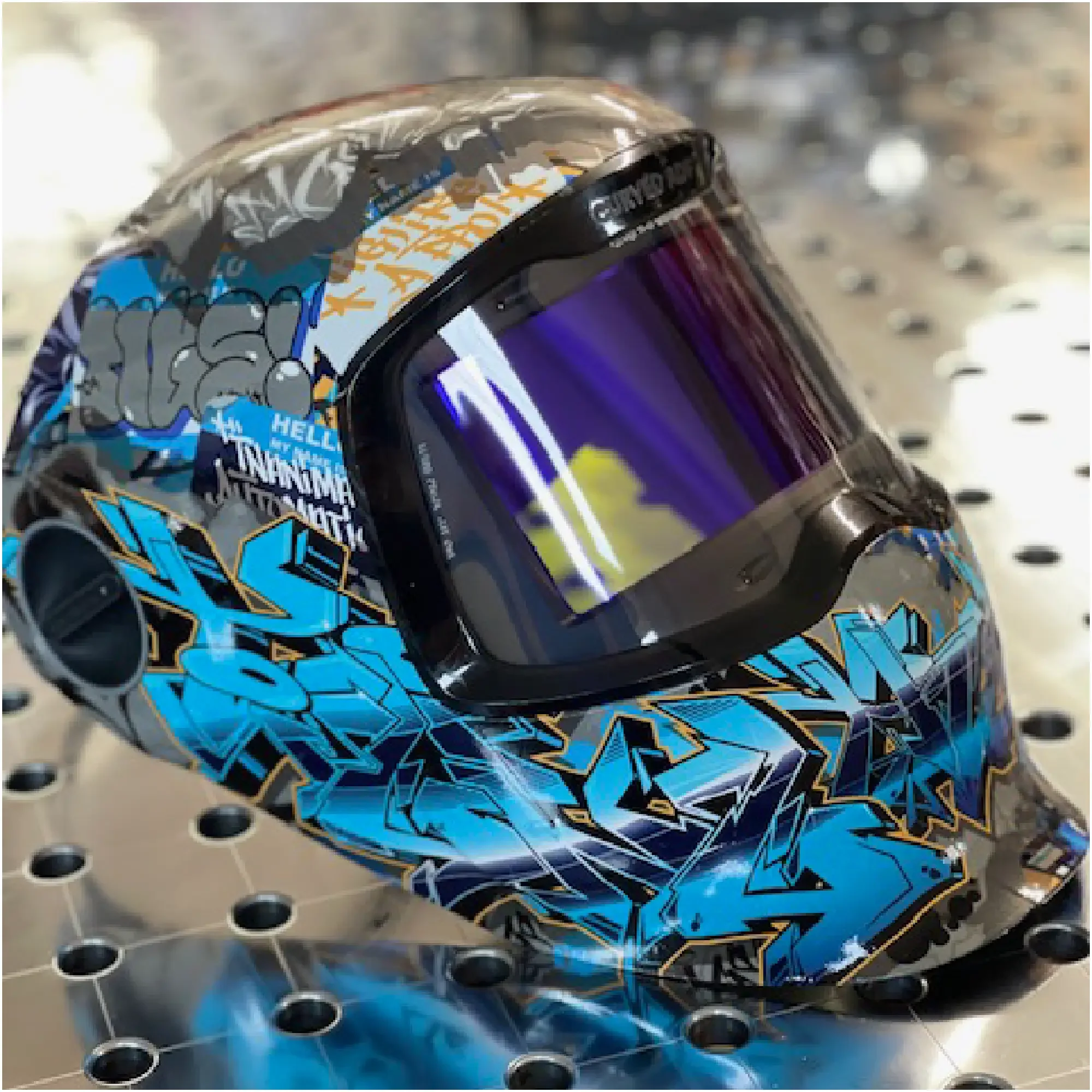 Tiging Them Softly™ Urban Tag welding helmet wrap — graffiti-inspired vinyl wrap with layered blue, orange, and silver street art graphics by IA-FAB.