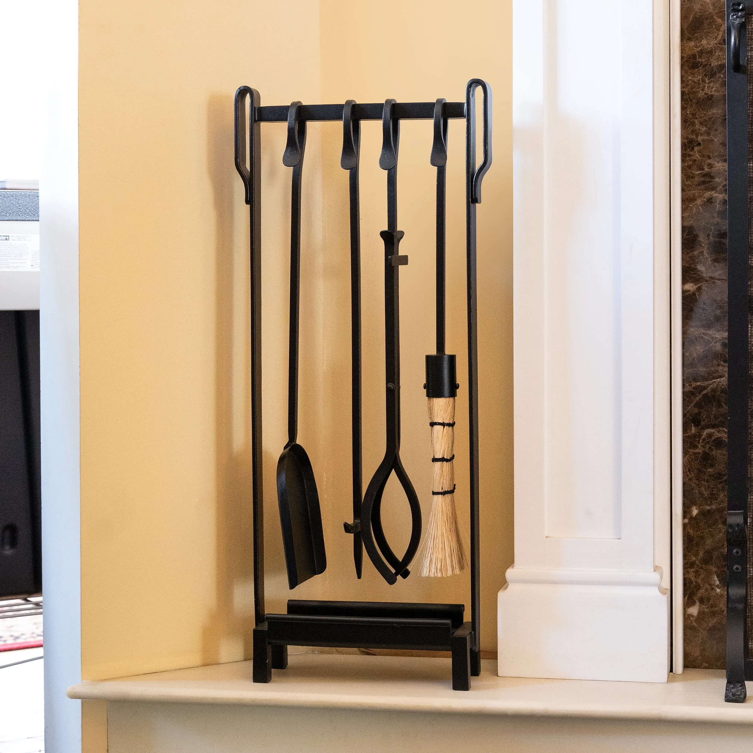 Set of black fireplace tools including a poker, tongs, a brush, and a shovel, arranged on a stand.