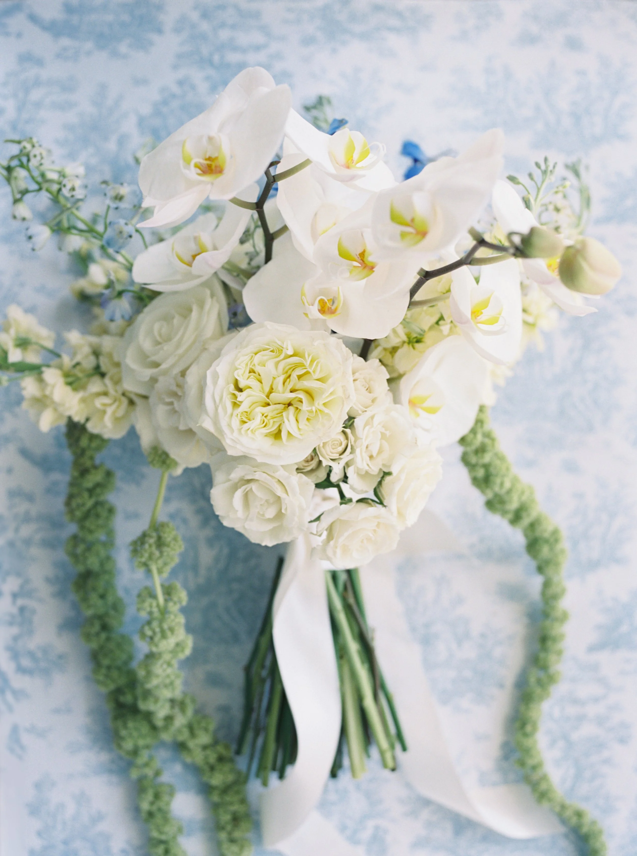Bouquet of white orchids, roses, and other white and green flowers on a light blue background.