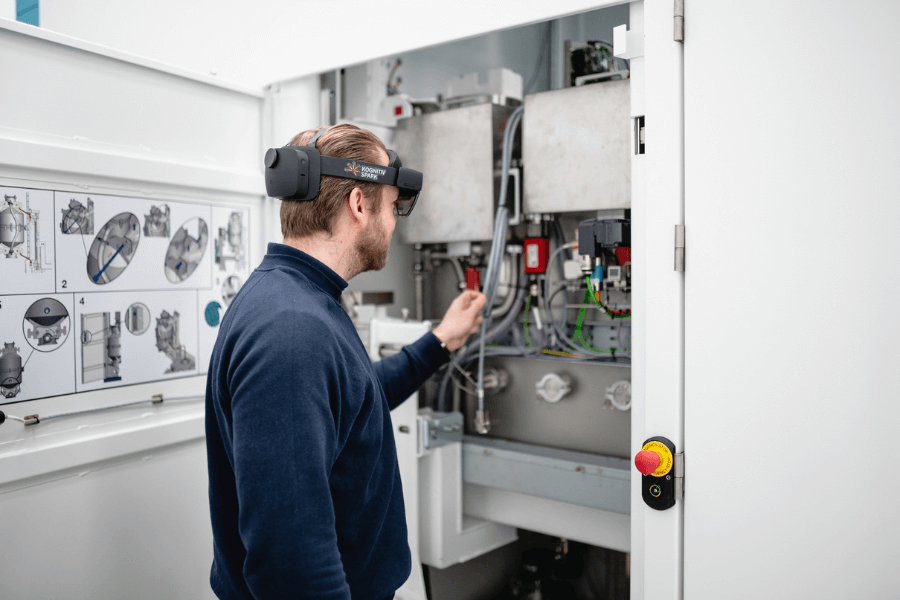 A man wearing a mixed reality headset and a navy blue sweater is working on an industrial electrical panel