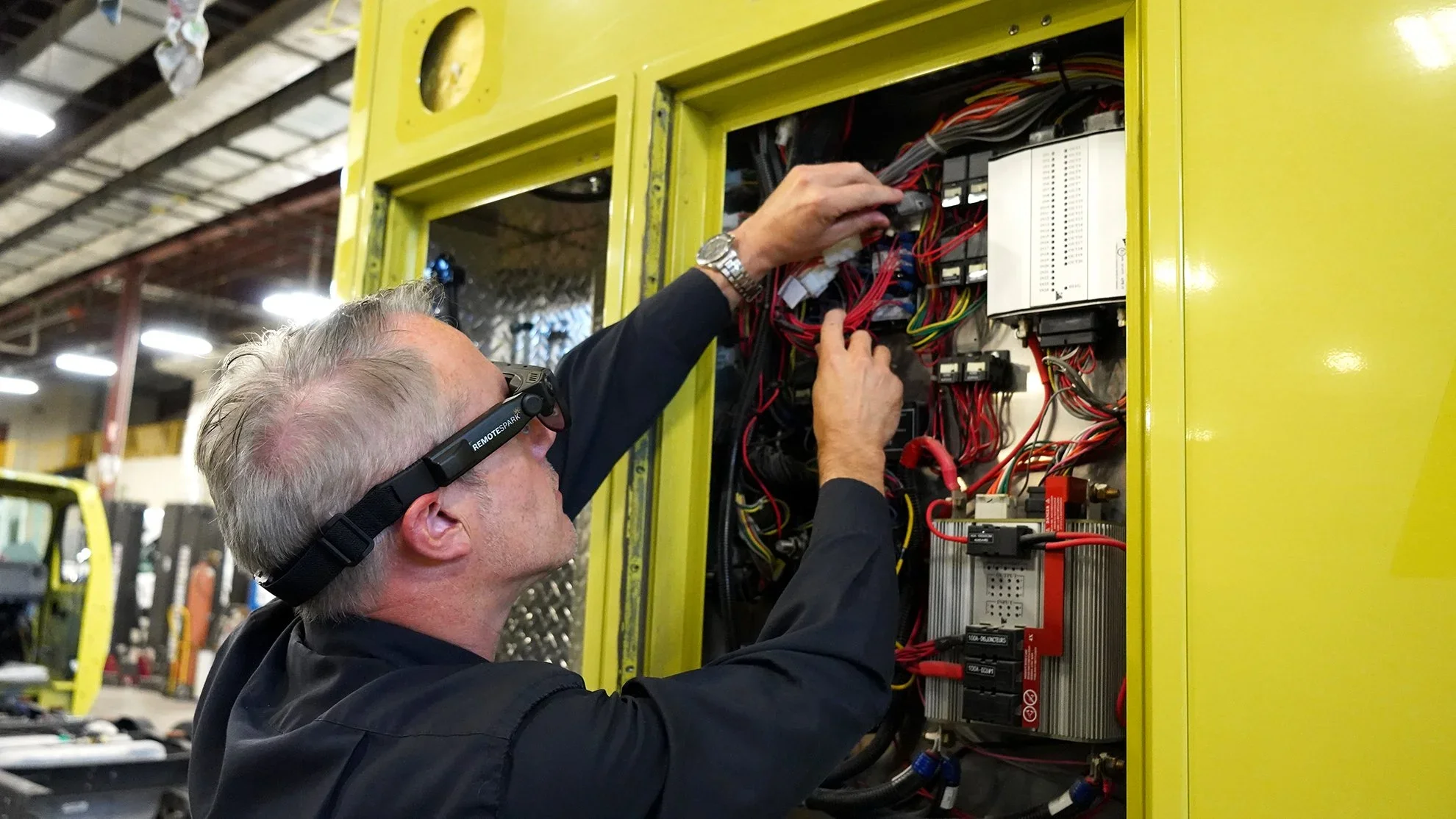 Man working on electrical wiring inside a yellow control panel in a warehouse using Augmented Reality glasses