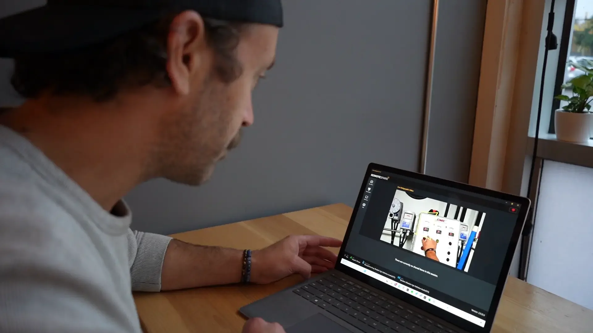 A man sitting at a wooden desk, looking at a laptop screen that displays a RemoteSpark call.