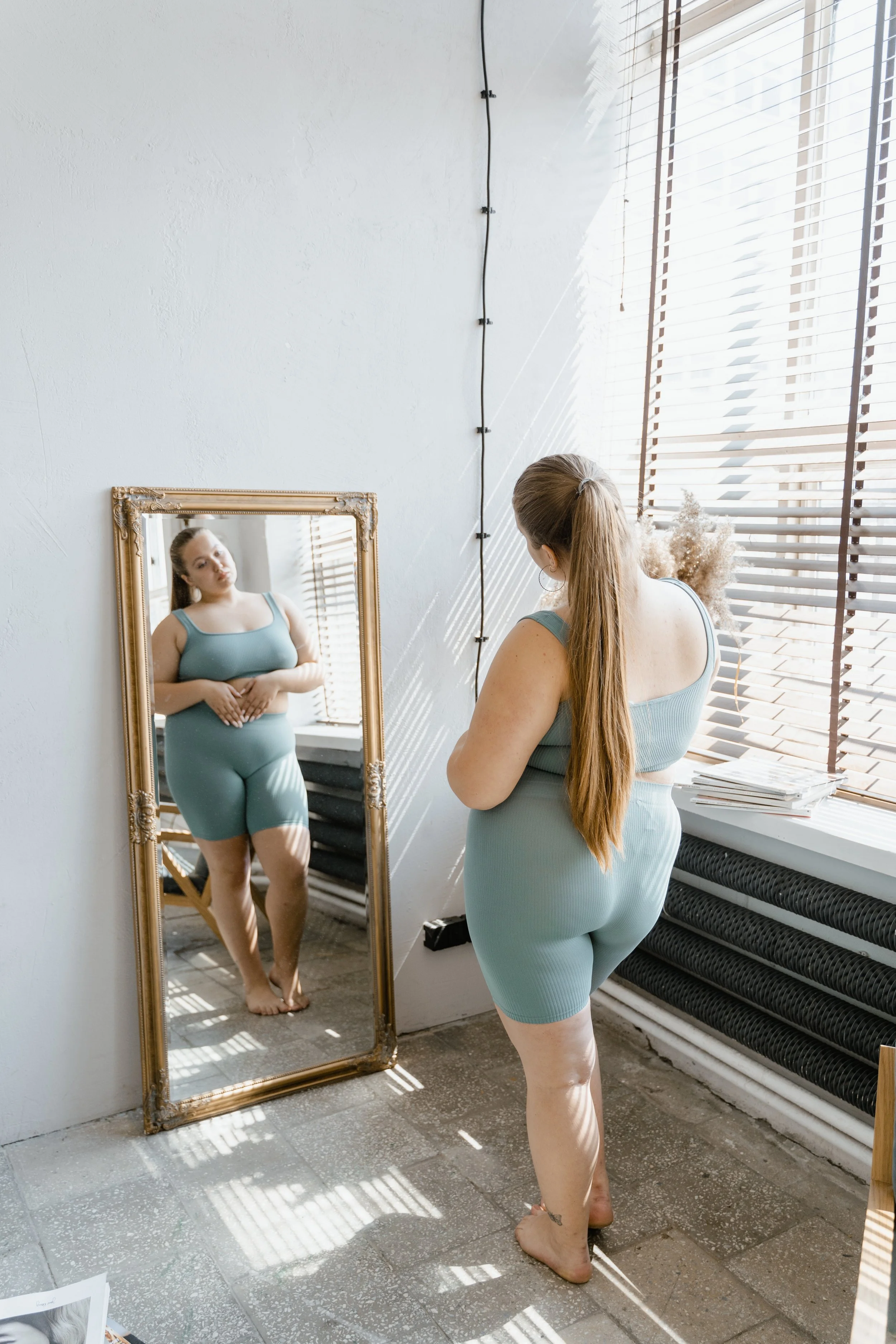 A plus size woman looking in a mirror at her body representing body neutrality. You may be curious and wonder - Can a therapist help me love my body? Therapy can be very powerful to assist in learning to accept yourself. 90402 | 90027 | 90266